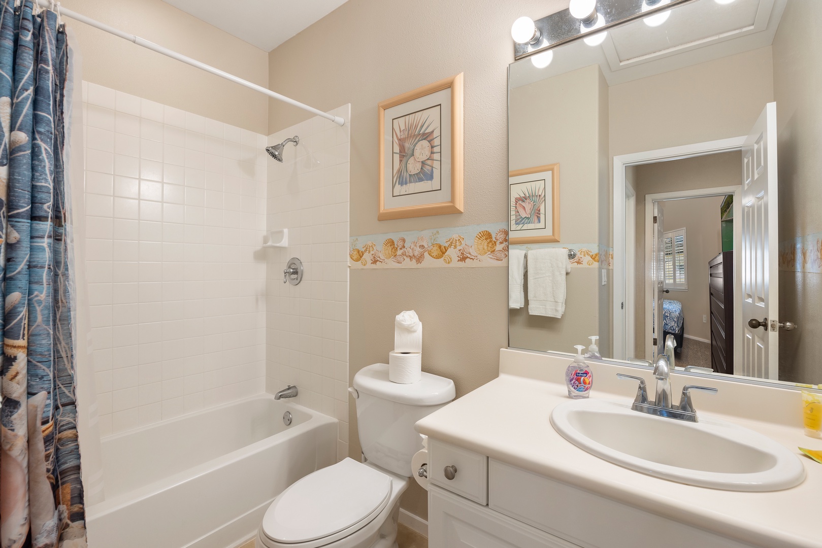 Your private bathroom features a relaxing tub-shower combo, seashell-themed décor, and vanity lighting for your morning routine.
