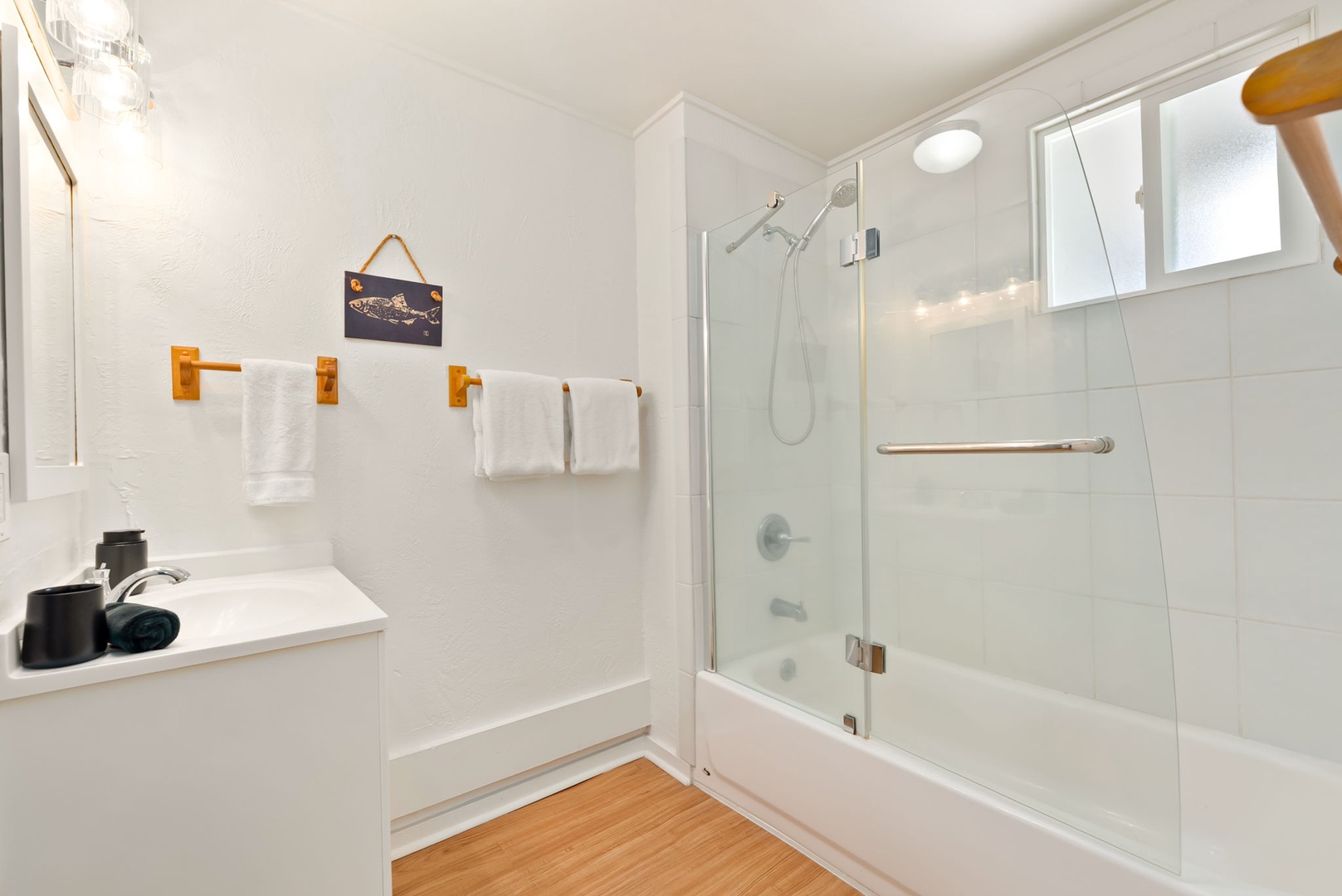Honolulu Vacation Rentals, Ho'okipa Villa - Your bright, clean bathroom features a tub-shower combo with glass doors, crisp white towels, and warm wood flooring for a cozy, refreshing retreat.