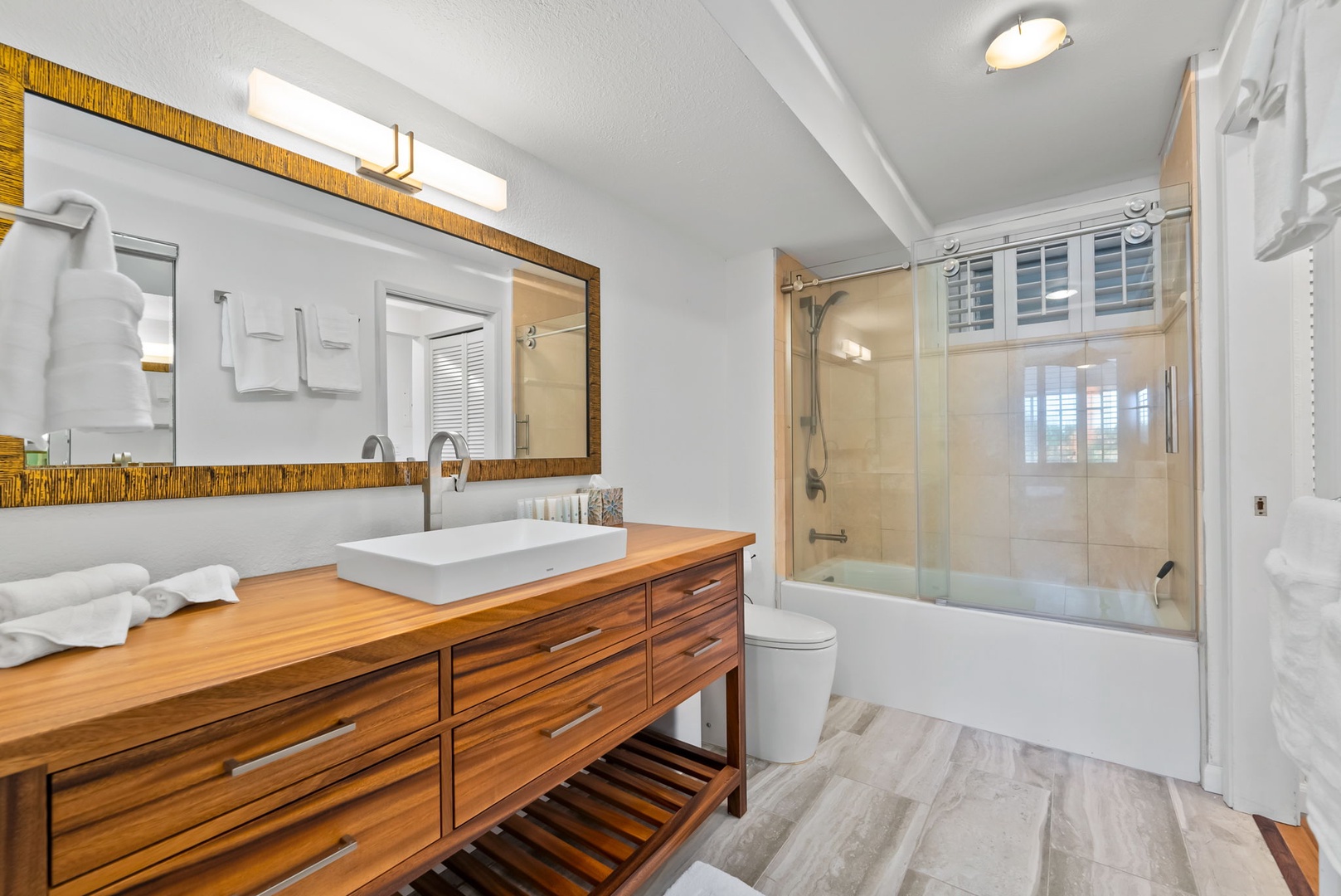 Honolulu Vacation Rentals, Colony Surf Retreat - Modern bathroom with a glass-enclosed walk-in shower, warm wood vanity, and ample storage—bringing comfort and functionality together.