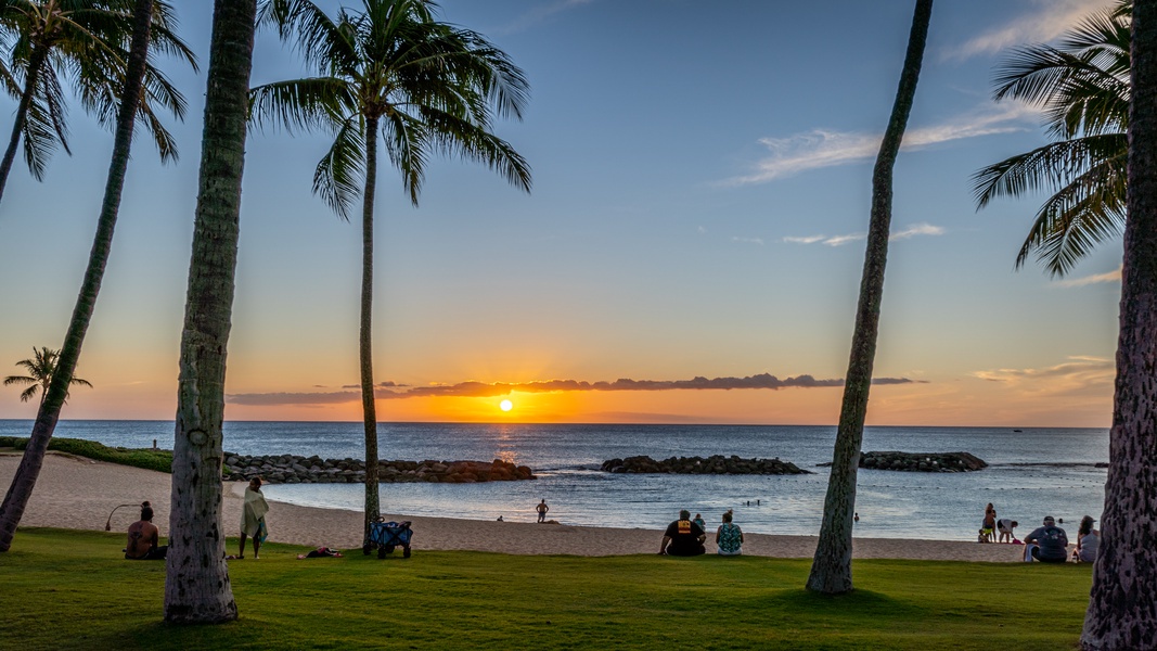 A stunning sunset paints the horizon golden over calm ocean waters, framed by swaying palms and a peaceful sandy beach—a beautiful tropical setting near the property.