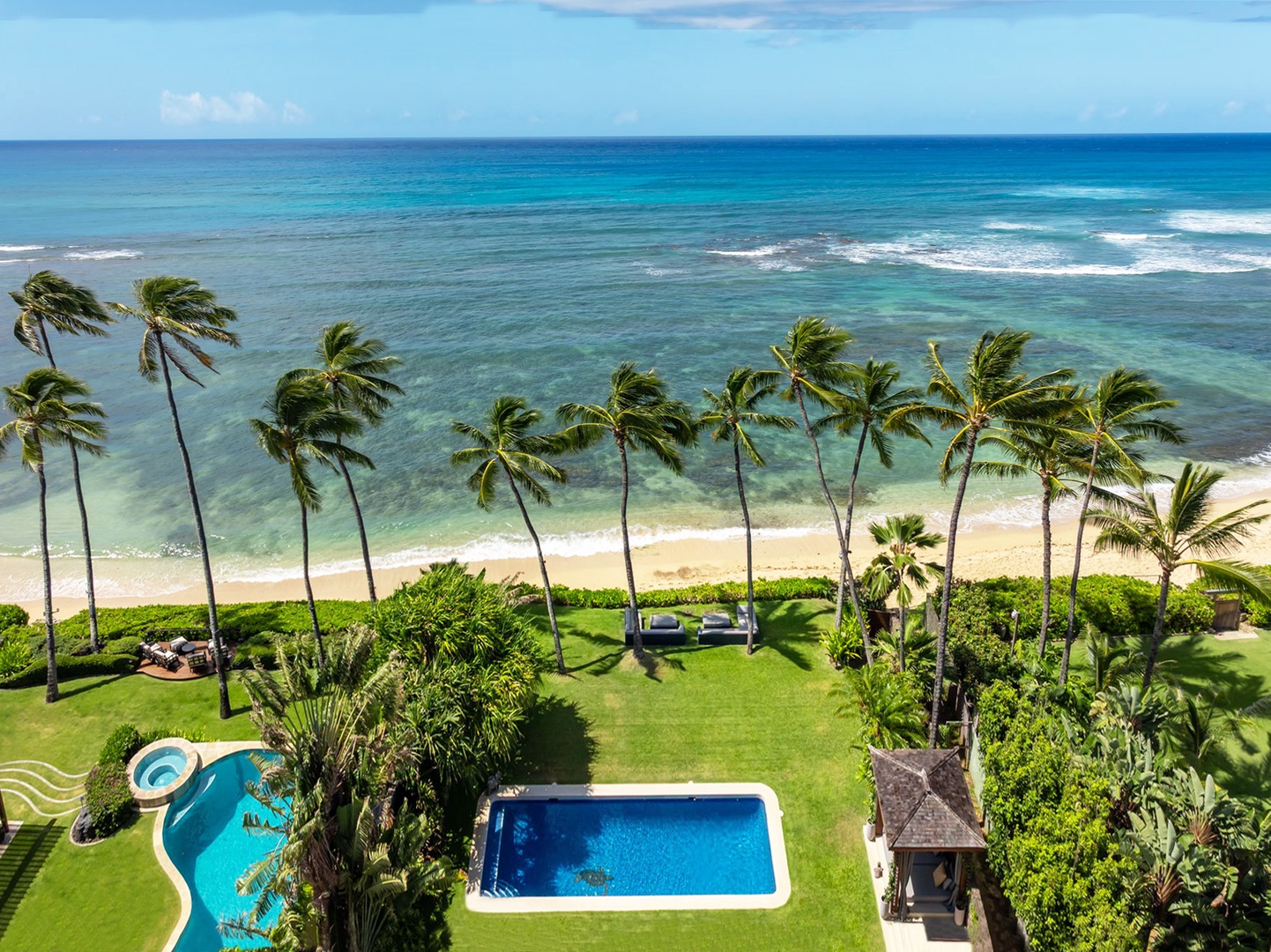 Honolulu Vacation Rentals, Diamond Head Beachfront Estate - Aerial view of beachfront property with private pool, tropical gardens, and sandy beach bordered by swaying palms and turquoise ocean waters.