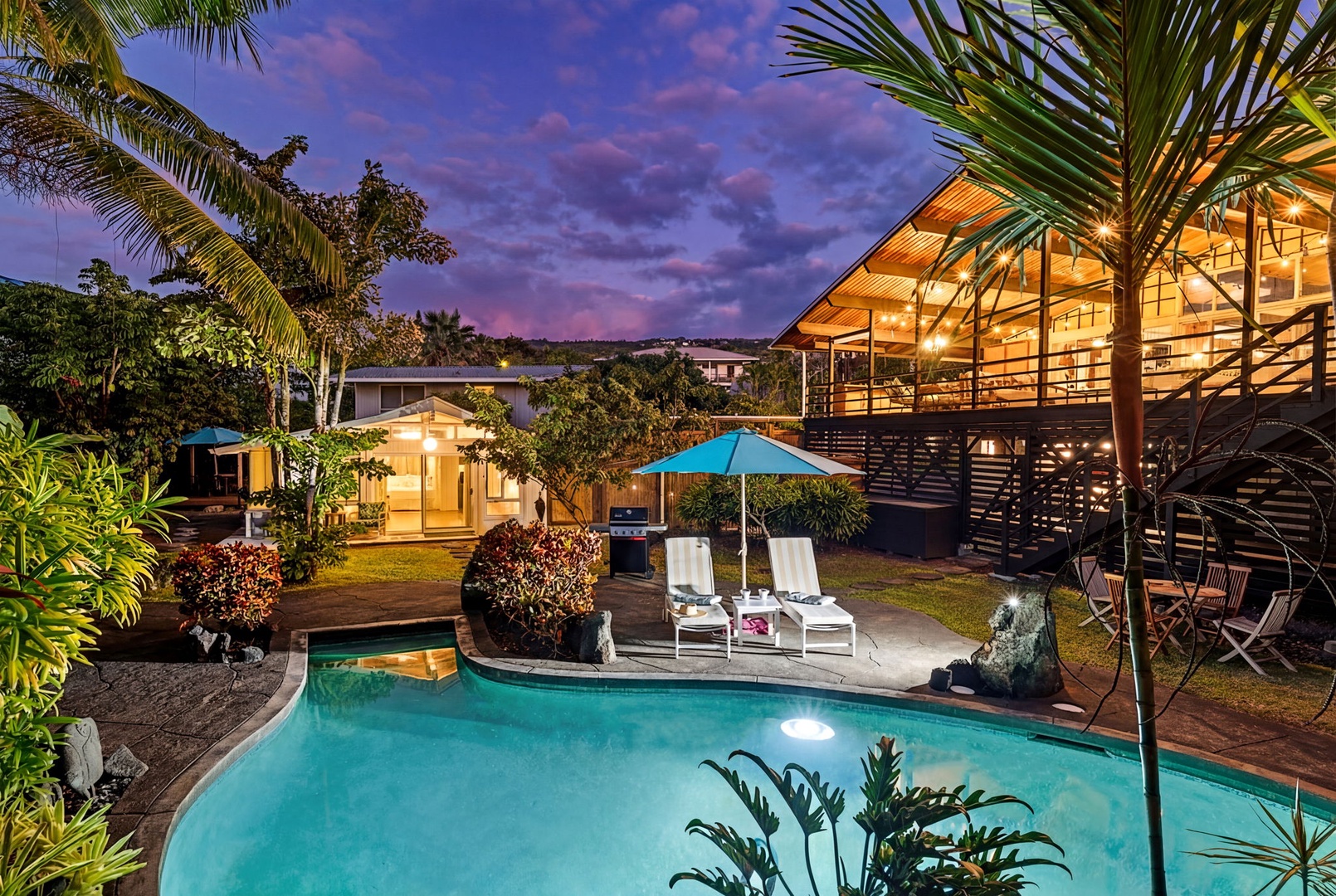 Kailua Kona Vacation Rentals, Mai Tai Manor - Tropical paradise awaits with illuminated swimming pool, palm trees, and modern architecture under a stunning sunset sky.
