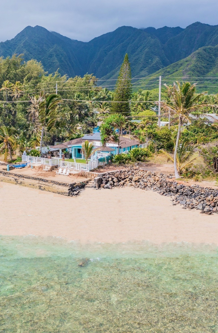 Hauula Vacation Rentals, Private Beach Paradise - A front-facing view of the home set directly on the sand, offering private beach access, turquoise snorkeling waters, and a dramatic backdrop of Sacred Falls and Jurassic Valley sea cliffs.