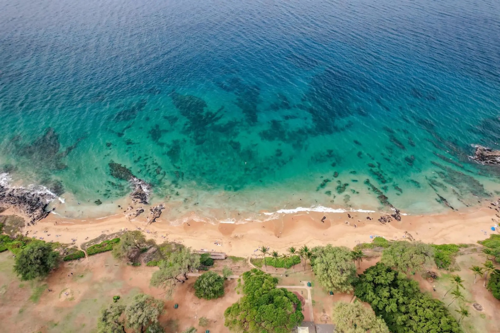 Kihei Vacation Rentals, Maui Kamaole E103 - Turquoise water and a scattering of sunbathers mark the beach from directly overhead.