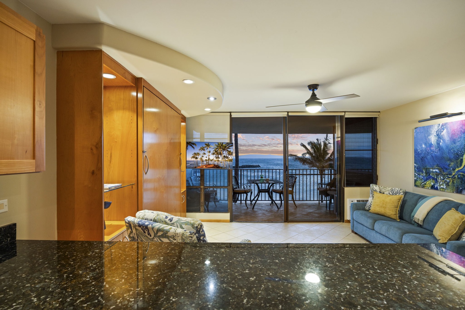 Wailuku Vacation Rentals, Milowai 310 - The floral armchair and the granite bar frame the same sliding doors, with the sunset and the lanai table just beyond.