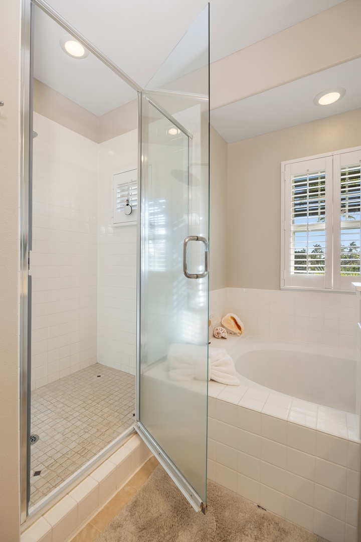 Unwind in your private spa-like bathroom featuring a spacious glass shower and luxurious soaking tub with serene garden views.