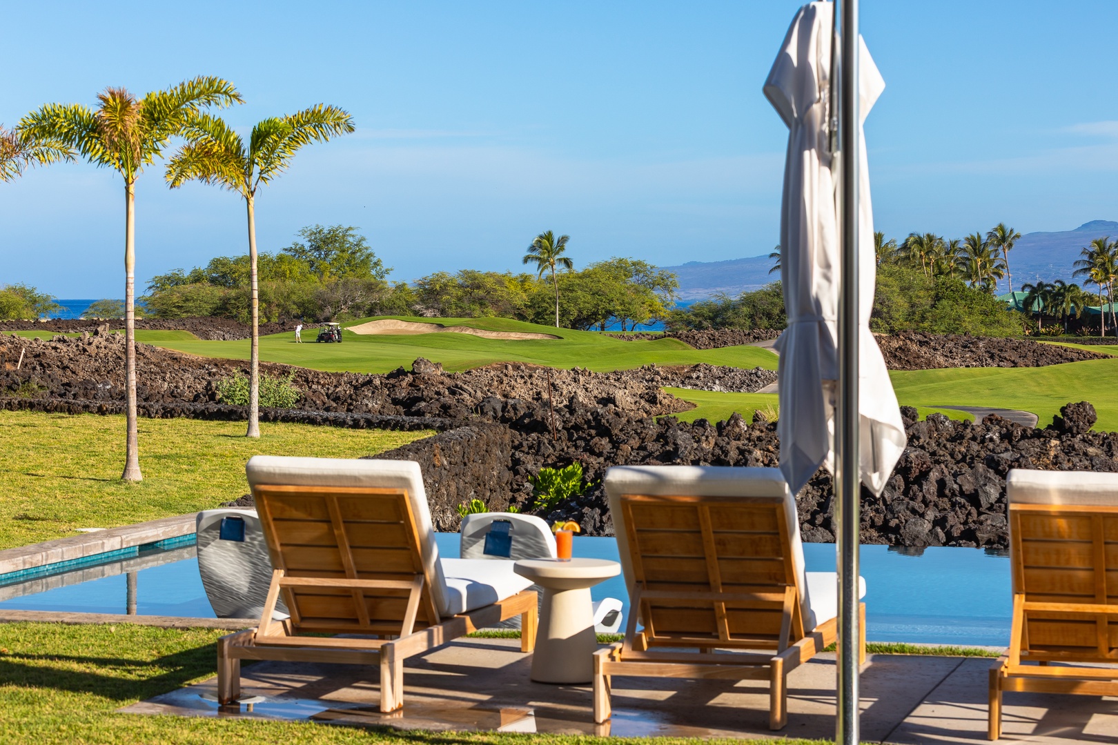 Kamuela Vacation Rentals, 5BD Mauna Lani Lux Ocean Estate (OE12) at One Ocean - Luxury poolside loungers overlook ocean views and championship golf greens surrounded by tropical palms and volcanic rock formations.