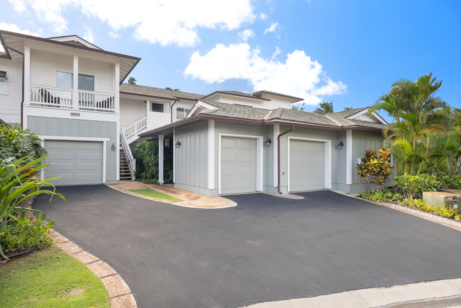 Elegant Hawaiian-style property with three-car garage and tropical landscaping under clear blue skies.