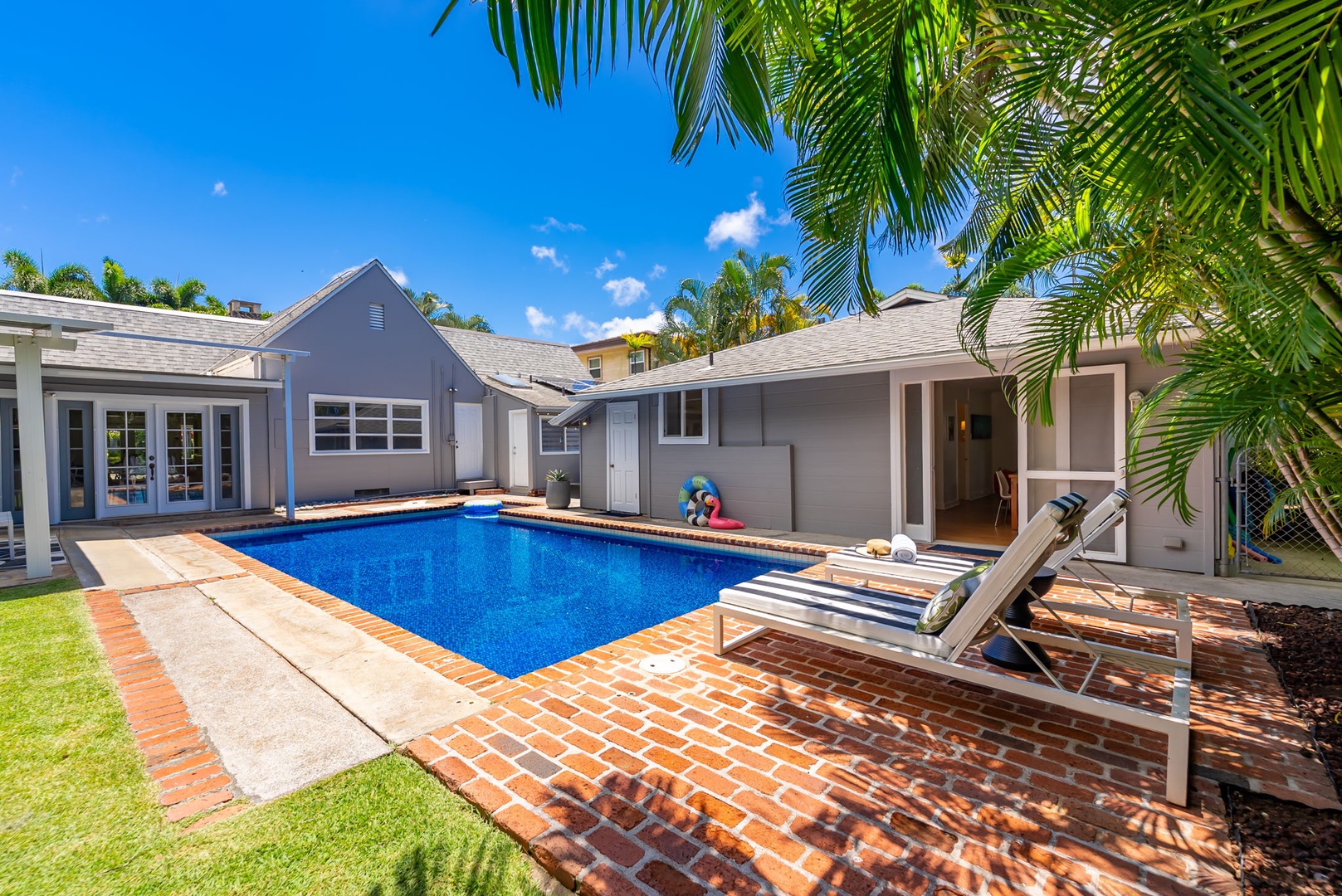 Honolulu Vacation Rentals, Ho'okipa Villa - Tropical backyard retreat with sparkling pool, sun loungers, and lush palms framing the property. Brick patio and verdant lawn complete your private outdoor escape.