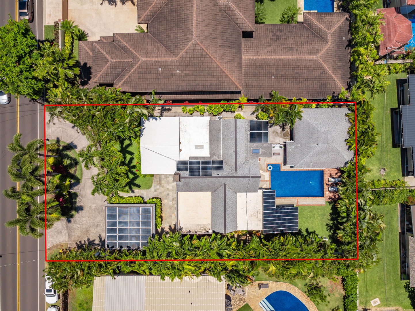 Honolulu Vacation Rentals, Ho'okipa Villa - Aerial view of a spacious residential property showcasing multiple rooftop solar panels, a private pool, and lush landscaped gardens within the marked property boundary.