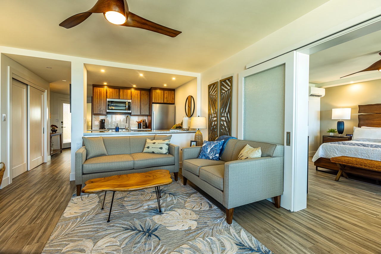 Kihei Vacation Rentals, Kamaole Beach Royal 610 - Two sofas circle a live-edge coffee table, the kitchen and primary suite both open just beyond.