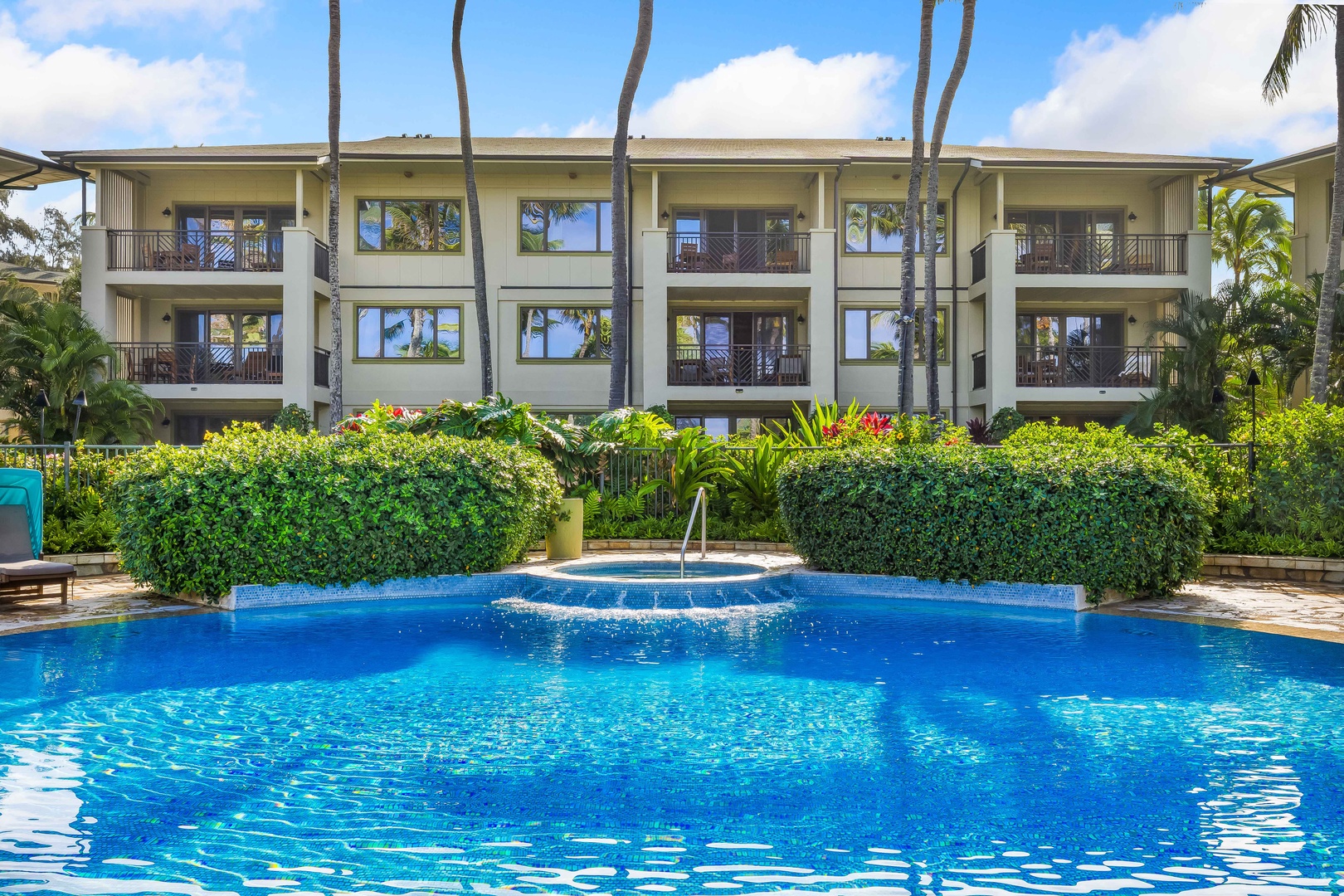 Kahuku Vacation Rentals, Turtle Bay Villas 209 - Tropical resort building with beautiful pool area surrounded by lush landscaping and palm trees.
