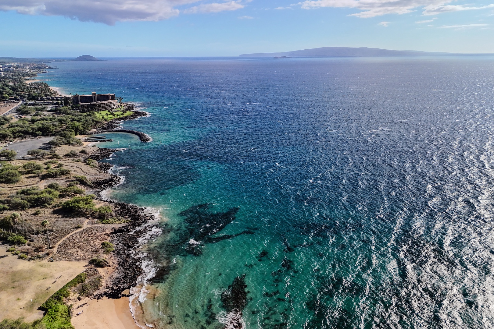 Kihei Vacation Rentals, Haleakala Shores A206 - A rock breakwater curls into the bay up the coast, with distant islands rising faint on the horizon.