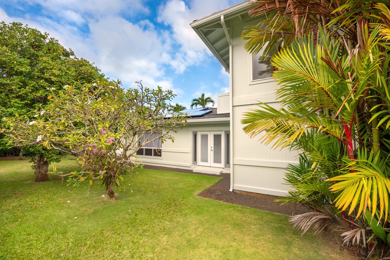 Princeville Vacation Rentals, Hihimanu House - A view of the house framed by tropical trees and plants.