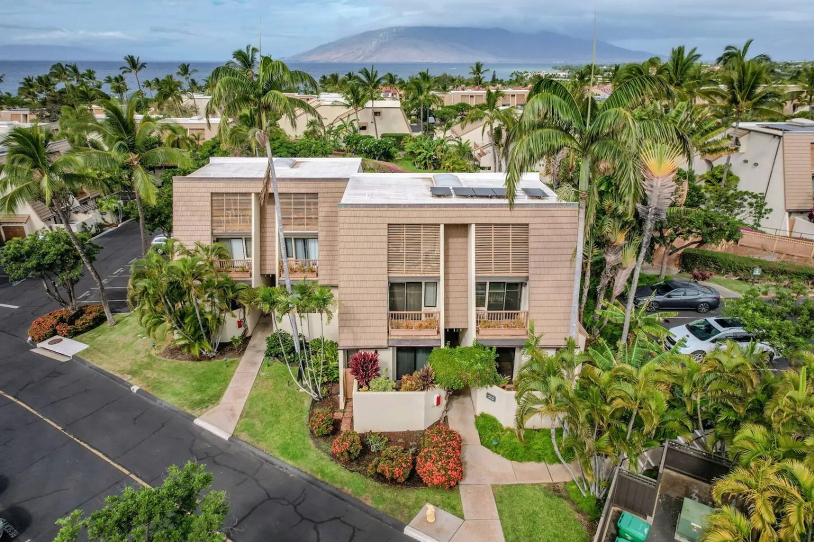 Kihei Vacation Rentals, Maui Kamaole E103 - Solar panels top the roofline, with the ocean and mountains stretching out behind the building.