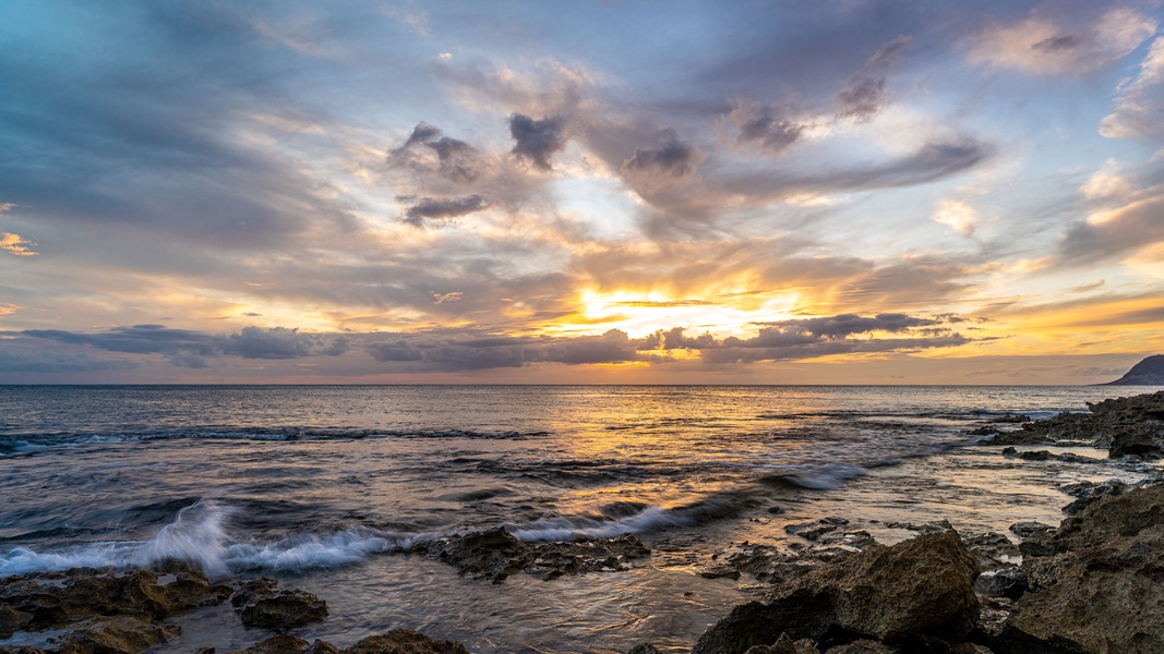Kapolei Vacation Rentals, Coconut Plantation 1150-2 - Golden sunset paints the sky over rocky coastline with gentle waves lapping the shore in this stunning natural landscape.