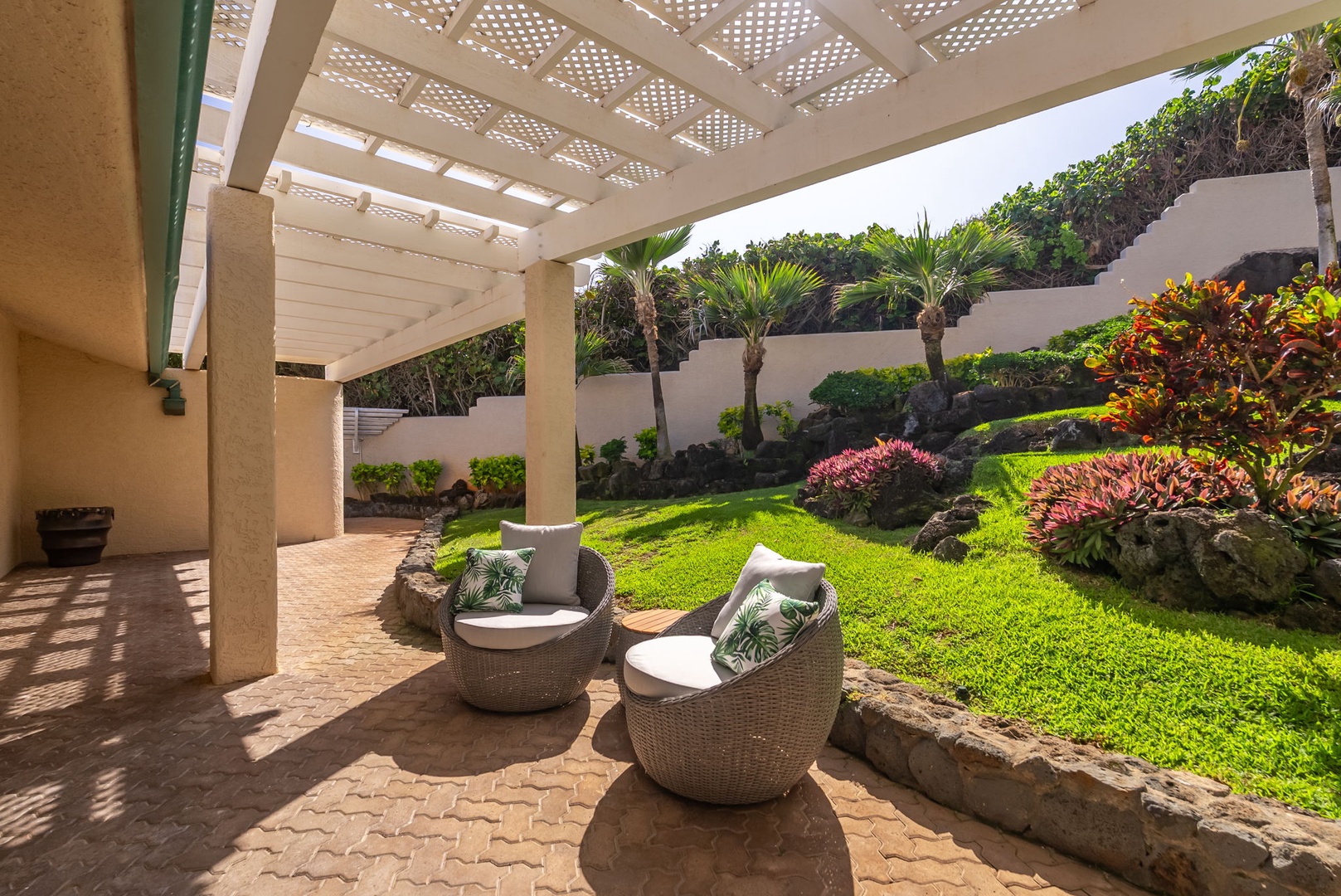 Honolulu Vacation Rentals, Black Point Ocean Villa - Garden oasis with comfortable wicker seating under a shaded pergola, surrounded by tropical palms and vibrant landscaping.
