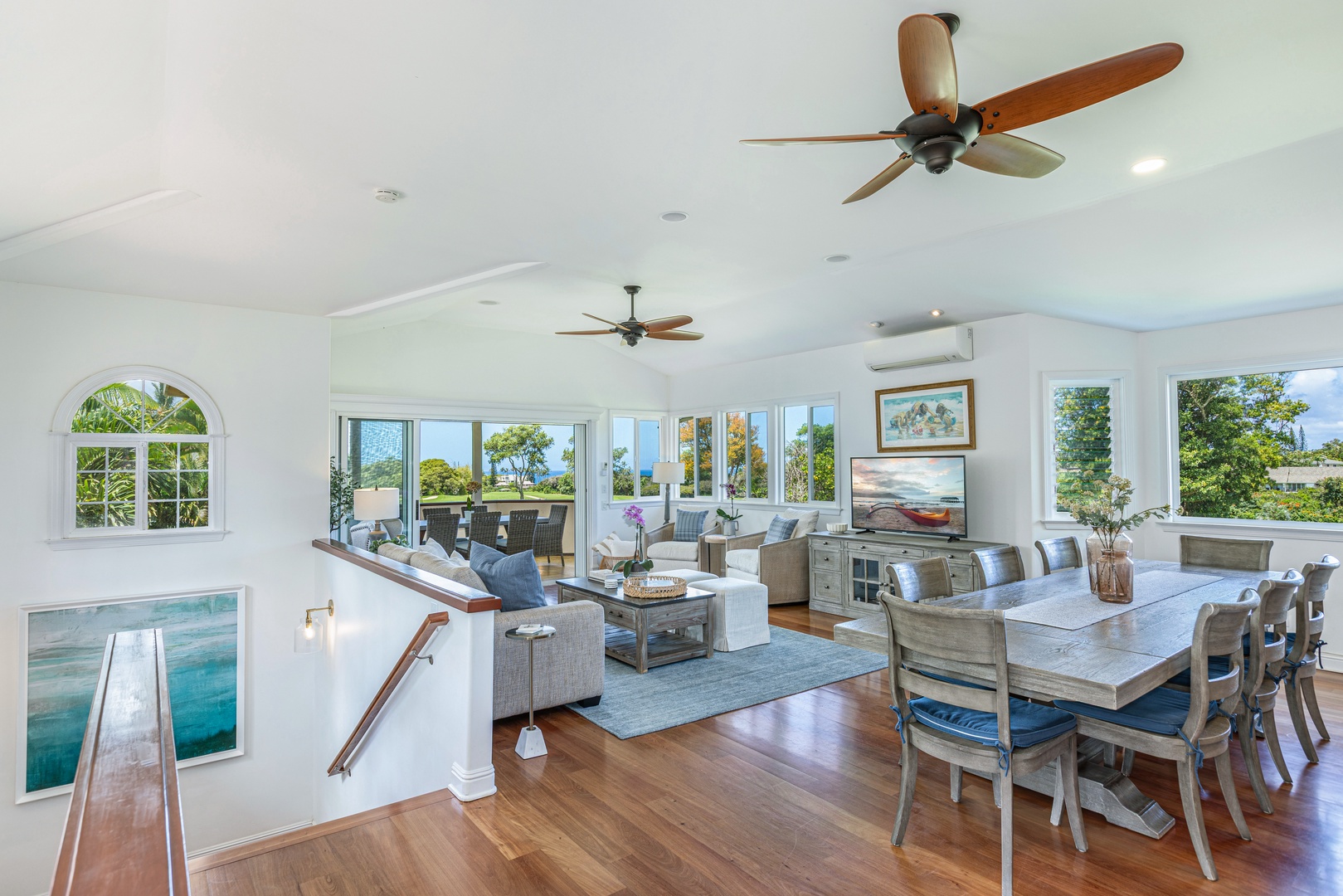 Princeville Vacation Rentals, Ohana Kamalani - Spacious upstairs lounge and dining area with wood floors, ceiling fans, and expansive windows framing lush views.