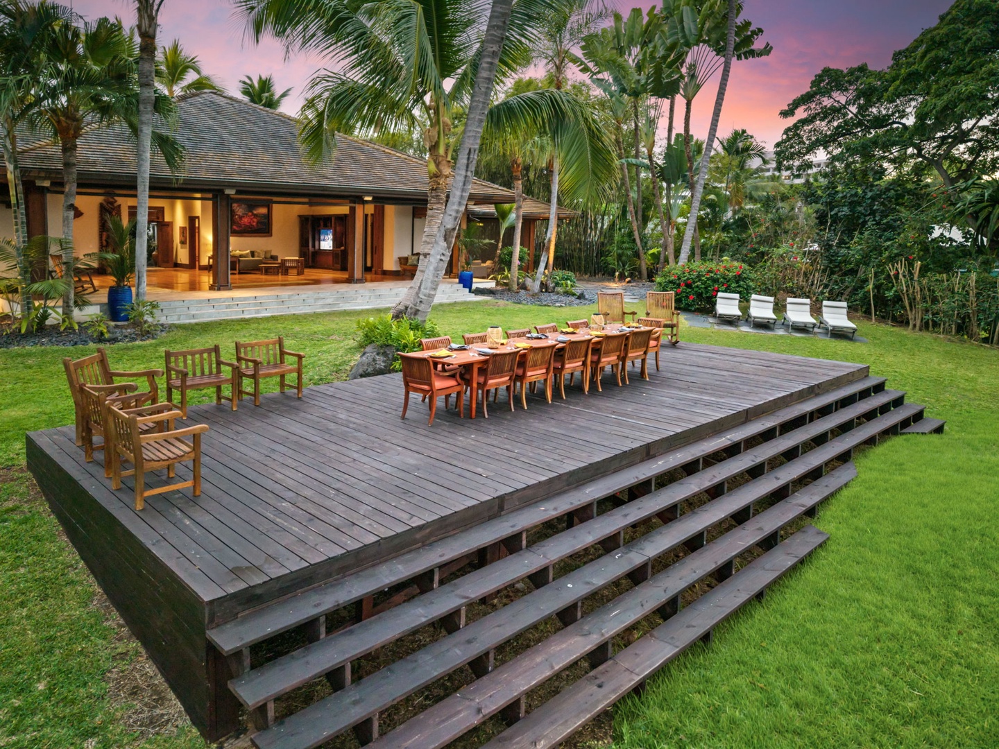 Kailua-Kona Vacation Rentals, Hahalua Bay Villa - Tropical villa surrounded by lush palm trees and landscaped gardens, featuring an elevated wooden deck with outdoor dining space beneath a colorful sunset sky.