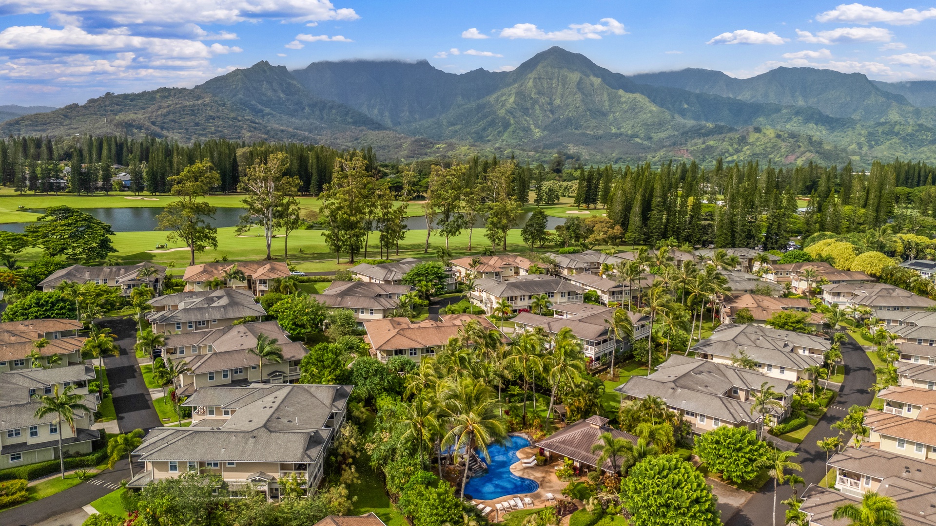 Princeville Vacation Rentals, Kaimana Villa - Aerial view of tropical resort community nestled beneath majestic mountains, featuring lush greenery and golf course surroundings.