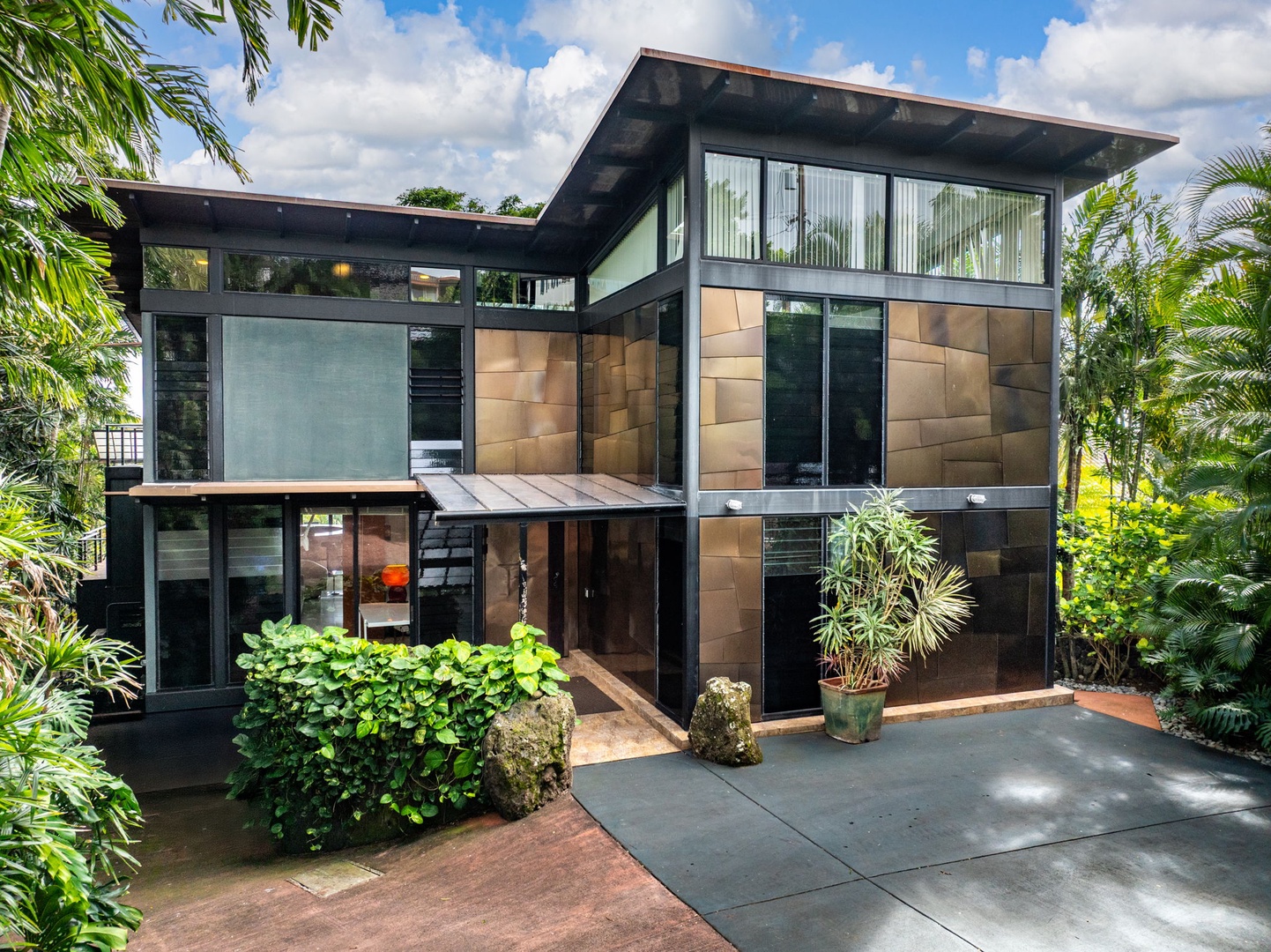 Honolulu Vacation Rentals, Tantalus Glass House (3 BD) - Modern tropical architecture featuring sleek lines and natural materials, nestled among lush palm trees and vibrant greenery in a peaceful setting.