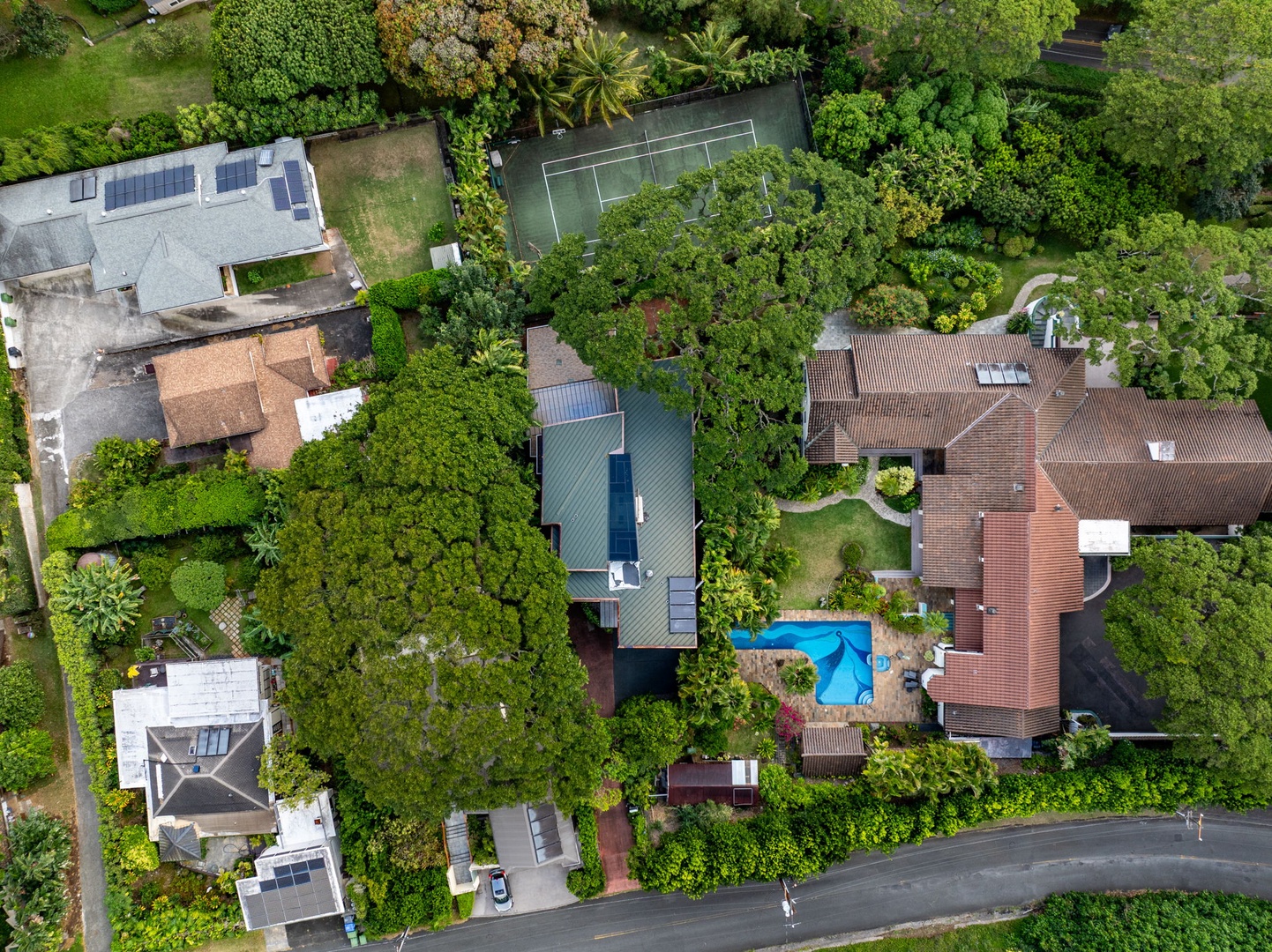 Honolulu Vacation Rentals, Tantalus Glass House (3 BD) - Aerial view of a lush residential neighborhood featuring properties with pools, tennis courts, and mature tropical landscaping.