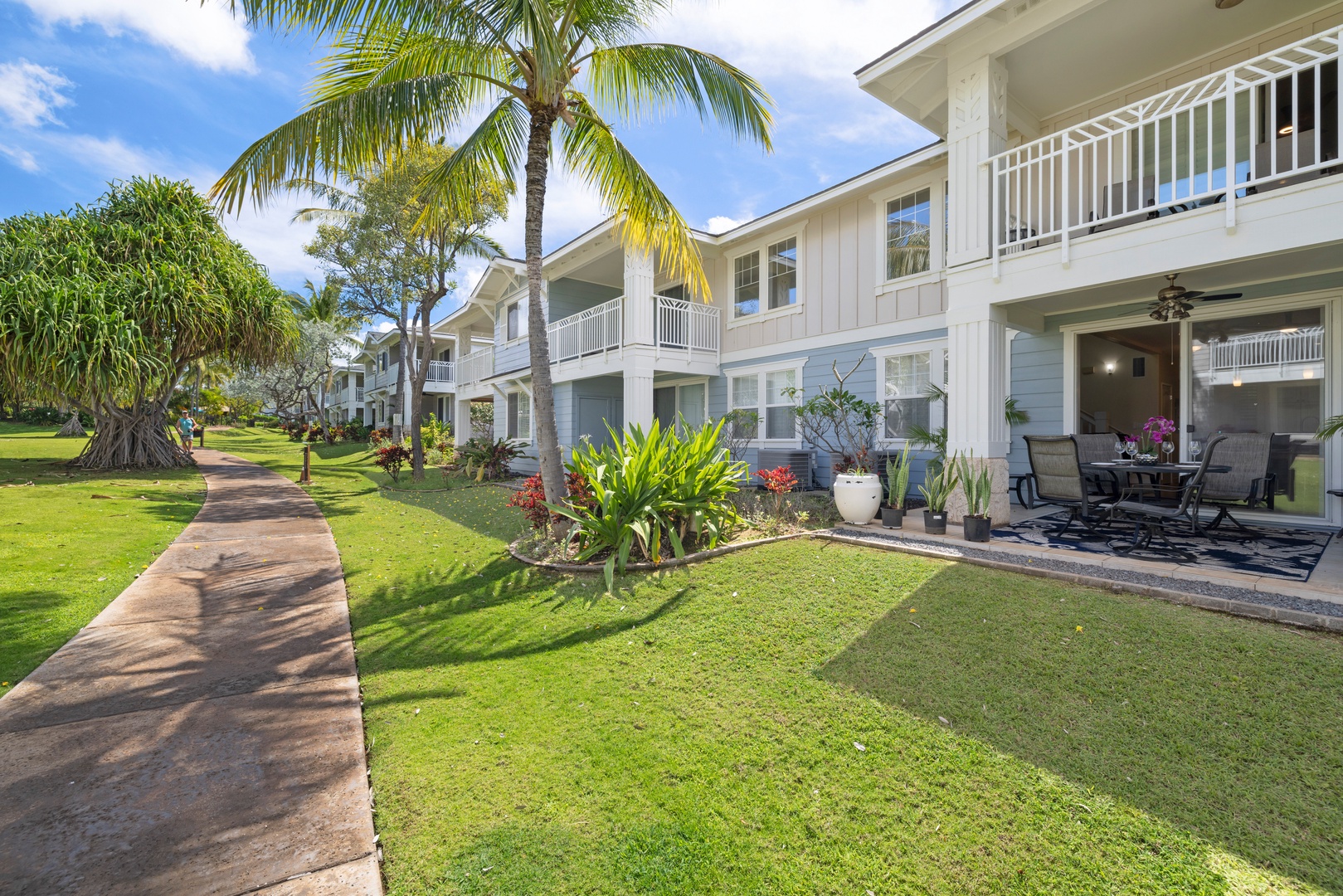 Multi-story vacation property featuring white buildings with balconies, tropical gardens, and walkways surrounded by lush palm trees and landscaping.