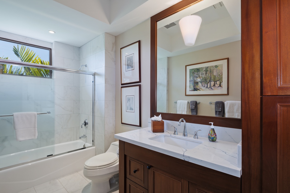 Kailua Kona Vacation Rentals, Fairways Villa 120A - Step into your elegant bathroom featuring marble countertops, warm wood cabinetry, and a relaxing tub-shower combo with natural light streaming in.