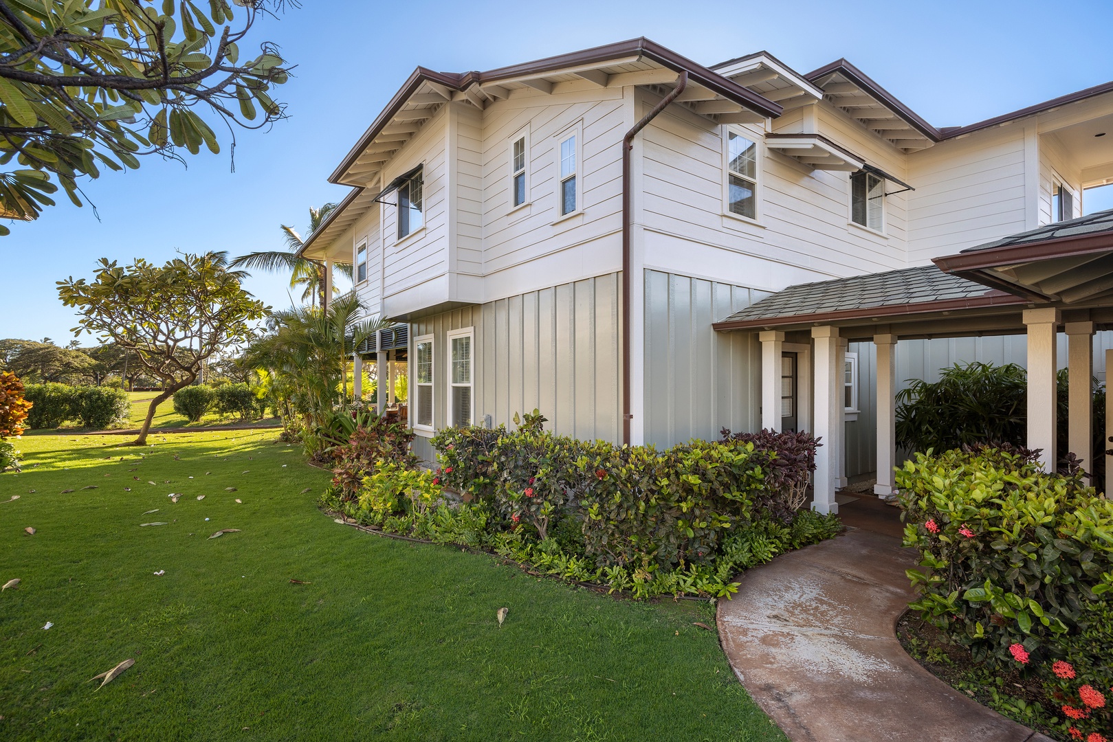 Elegant two-story property featuring pristine white exterior, mature tropical landscaping, and expansive green lawn surrounding the building.