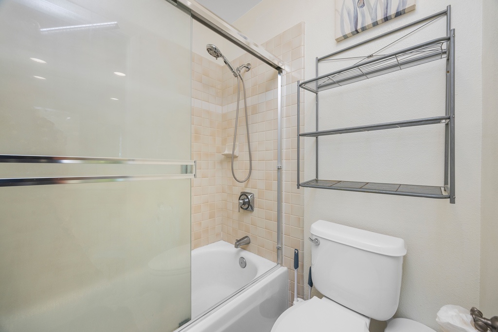 Refresh in your bright, modern bathroom featuring a glass-enclosed tub-shower combo and convenient built-in storage shelving for all your essentials.
