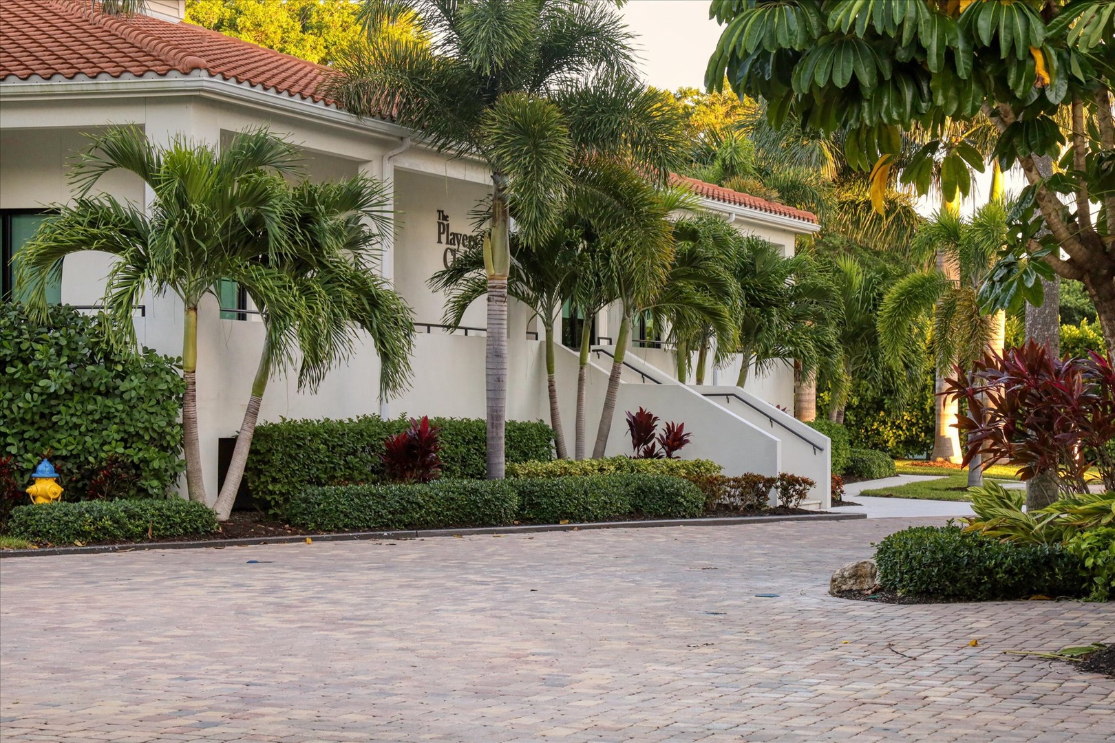 Elegant resort-style property featuring Mediterranean architecture, lush tropical landscaping, and pristine paved courtyards surrounded by swaying palms.