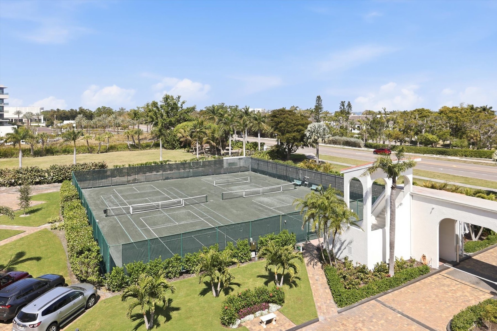 Aerial view of tennis courts surrounded by tropical gardens and parking areas within the property grounds.
