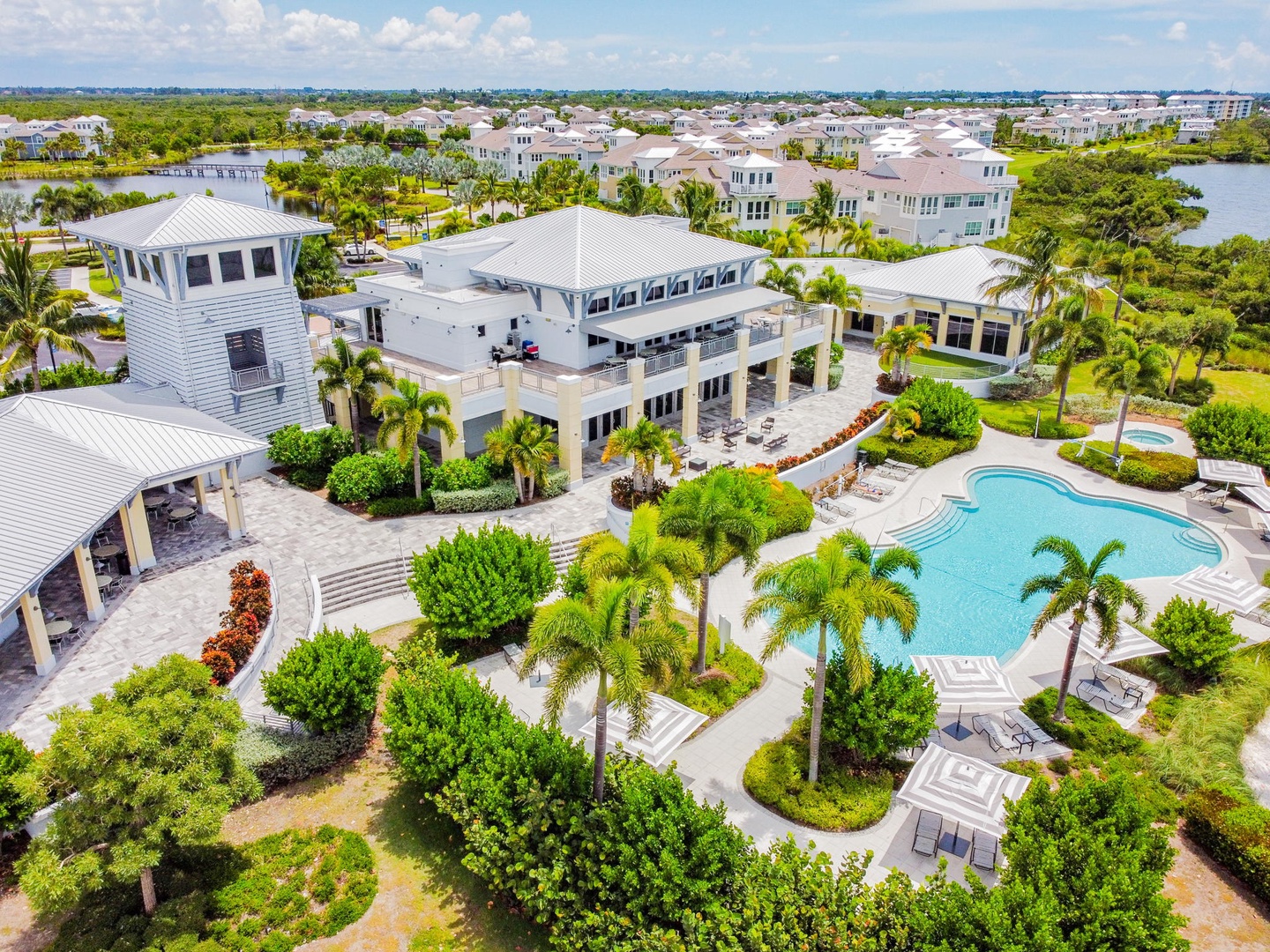 Aerial view of an elegant resort featuring multiple buildings, lush tropical gardens, and a sparkling swimming pool surrounded by palm trees.