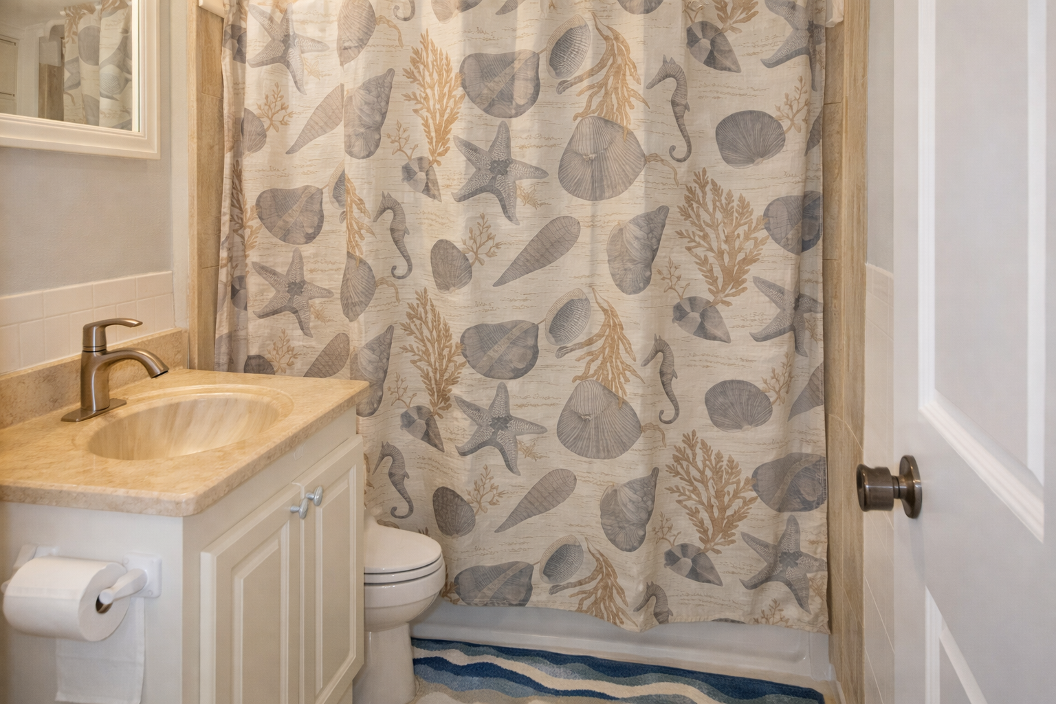 Full bathroom features coastal-themed décor with seashell shower curtains and warm beige tones.