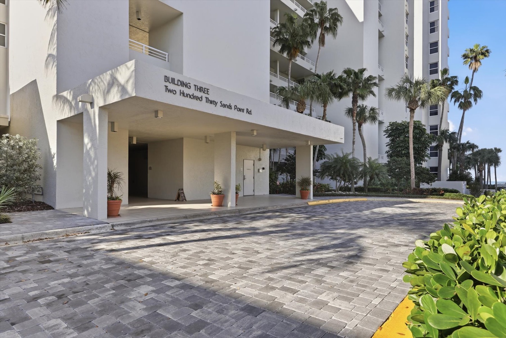 Modern building entrance with covered drop-off area and tropical landscaping creates a welcoming arrival experience.