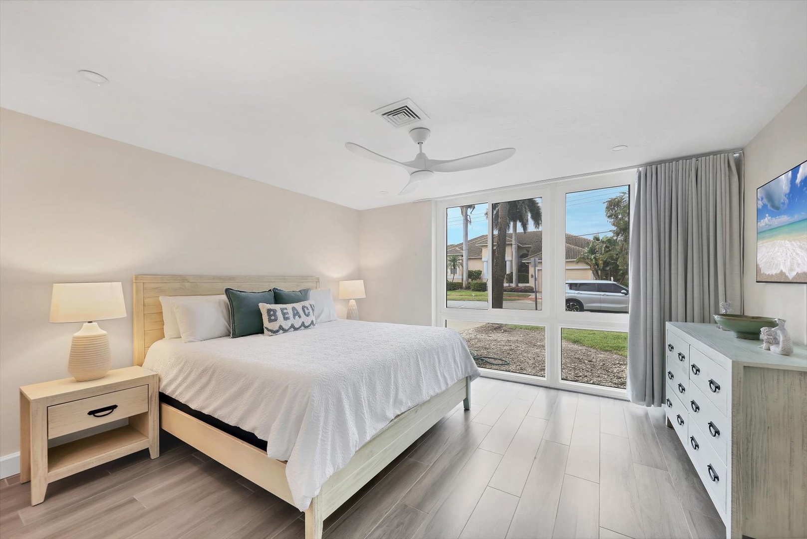 Unwind in your peaceful bedroom featuring a comfortable bed, natural light streaming through large windows, and calming coastal decor.