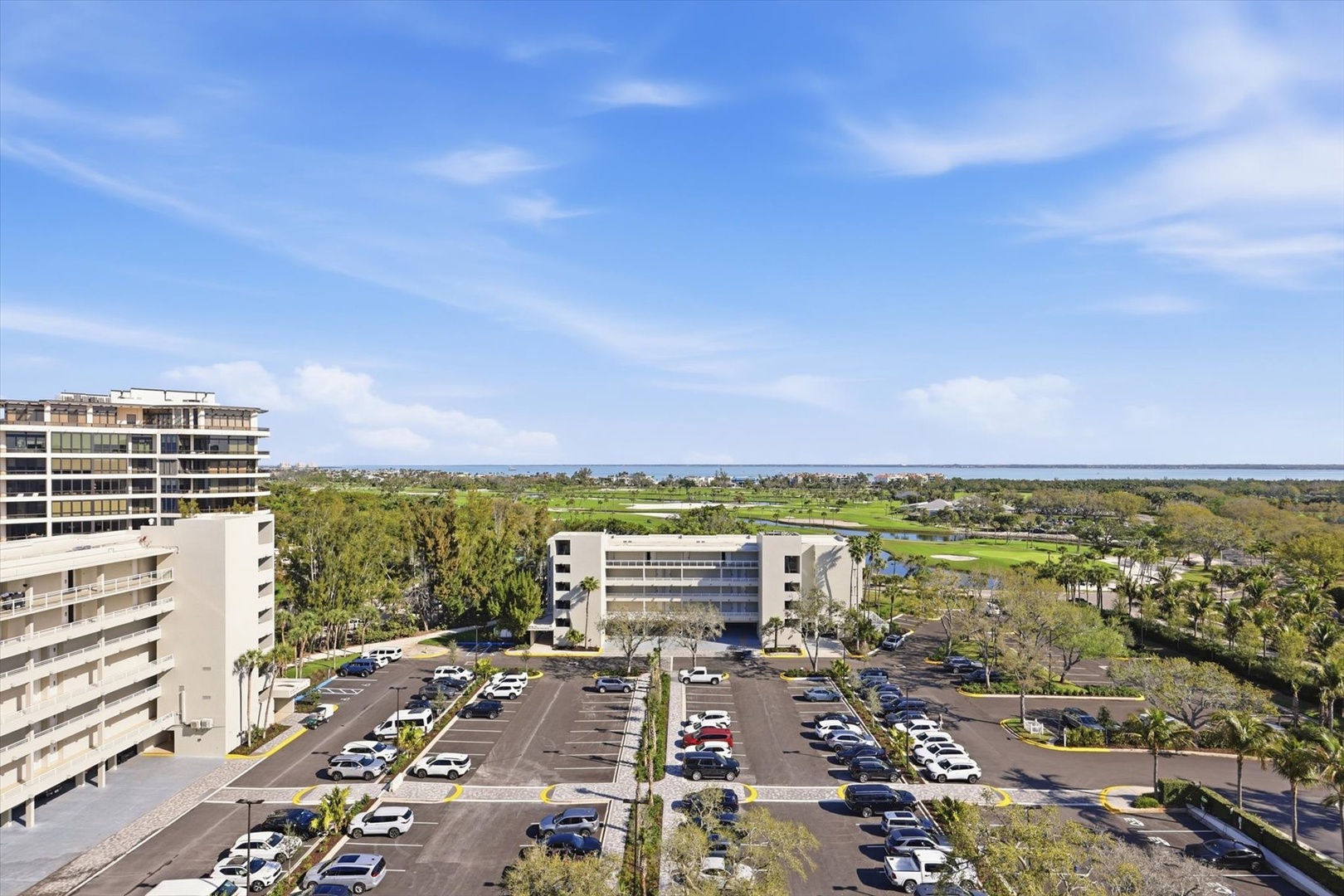 Elevated view of the property complex with expansive parking and surrounding green landscapes under clear blue skies.