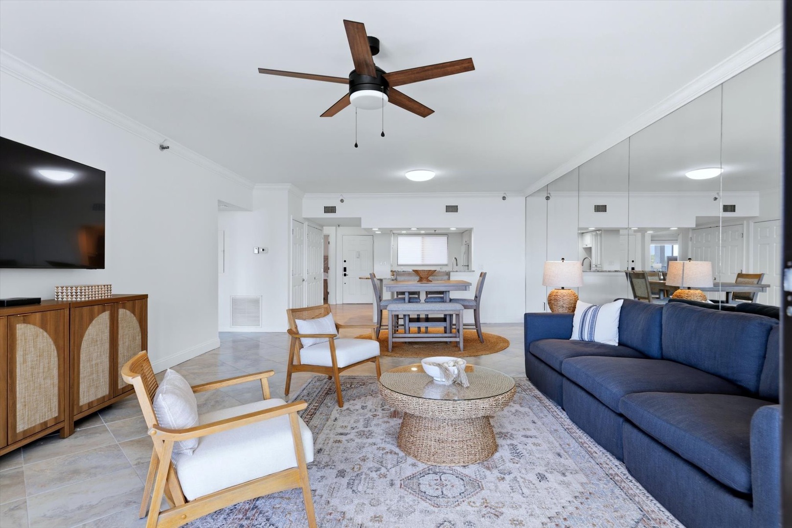 Unwind in your stylish open-plan living space featuring a plush navy sofa, coastal-inspired furnishings, and warm wood accents that create the perfect beach retreat ambiance.