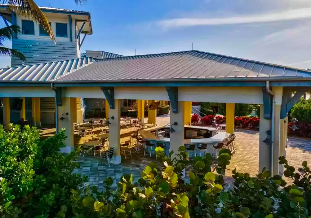 Open-air dining pavilion with tropical landscaping and colorful resort buildings in a Caribbean-style setting.