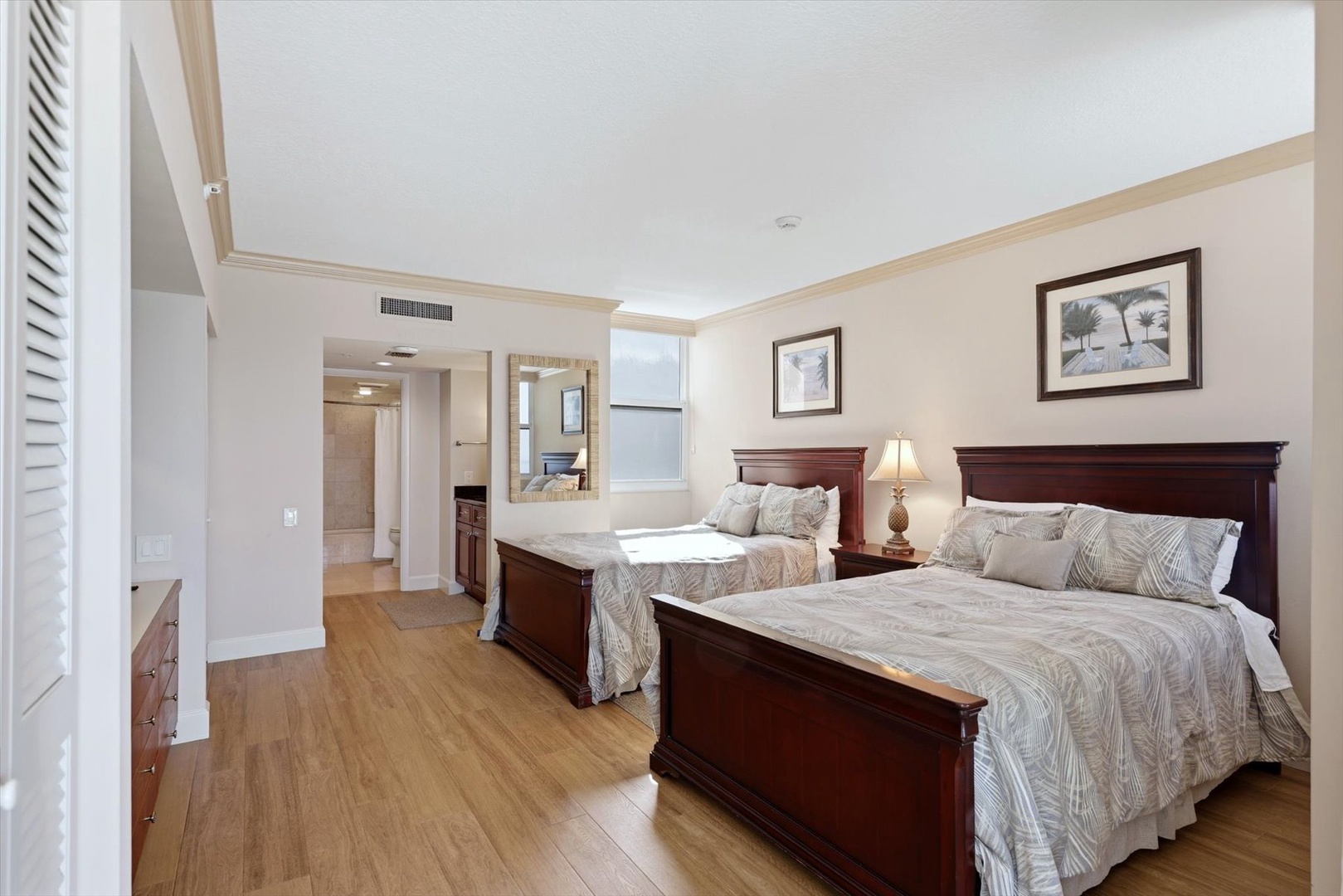 Your spacious bedroom features two comfortable beds with tropical-themed linens, warm hardwood floors, and abundant natural light for restful nights.