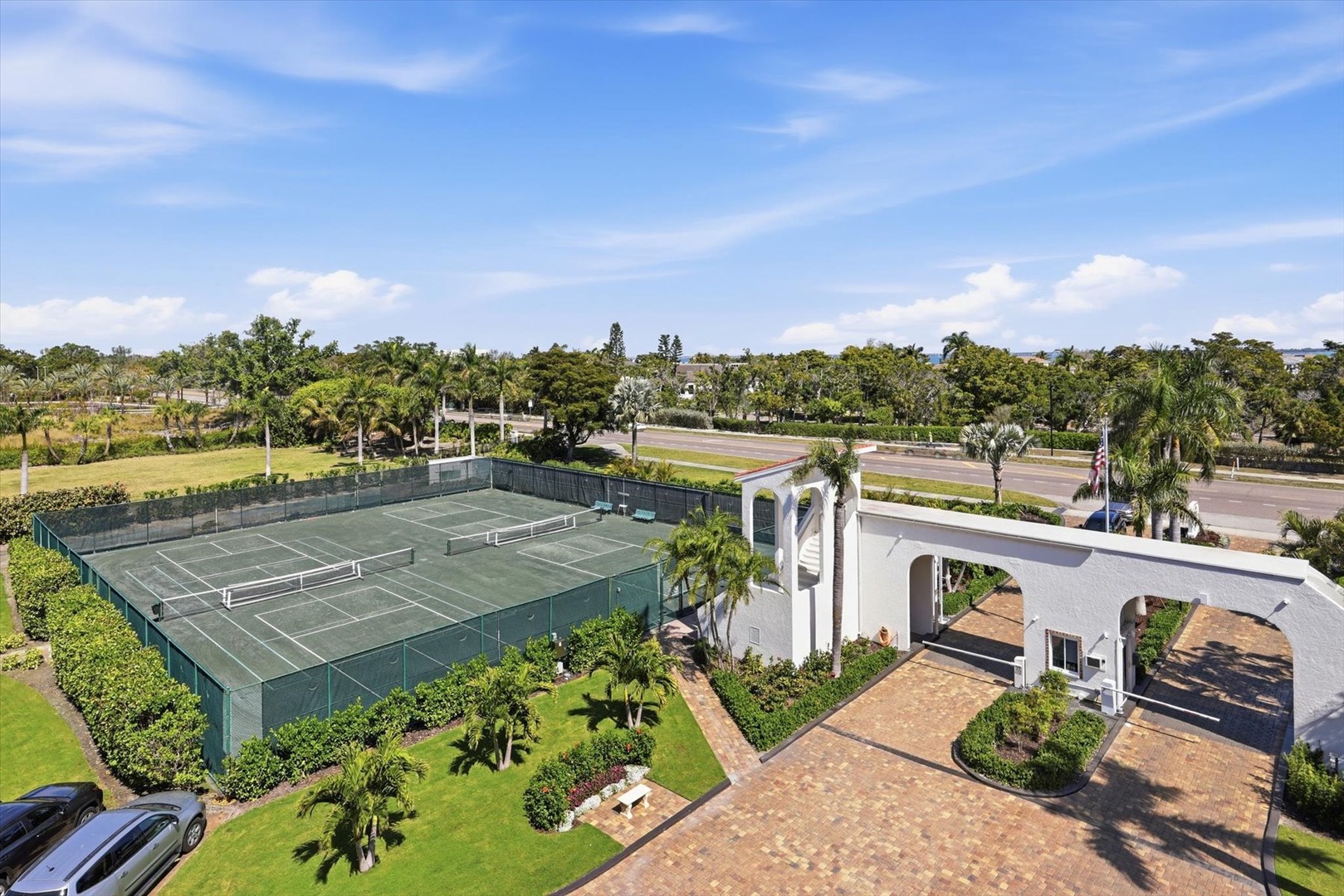 Tropical resort featuring private tennis courts surrounded by lush palm trees and manicured lawns in sunny daytime setting.