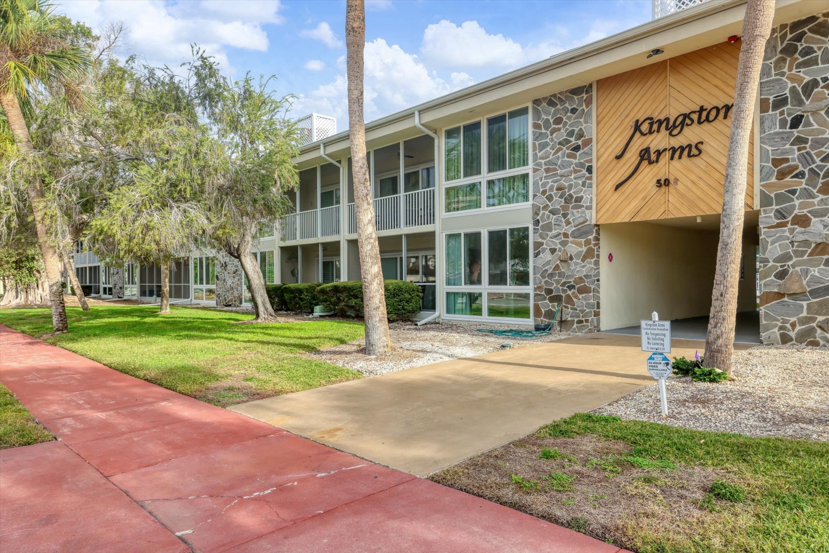 Kingston Arms property welcomes guests with stone facade, tropical landscaping, and convenient parking in a peaceful residential setting.