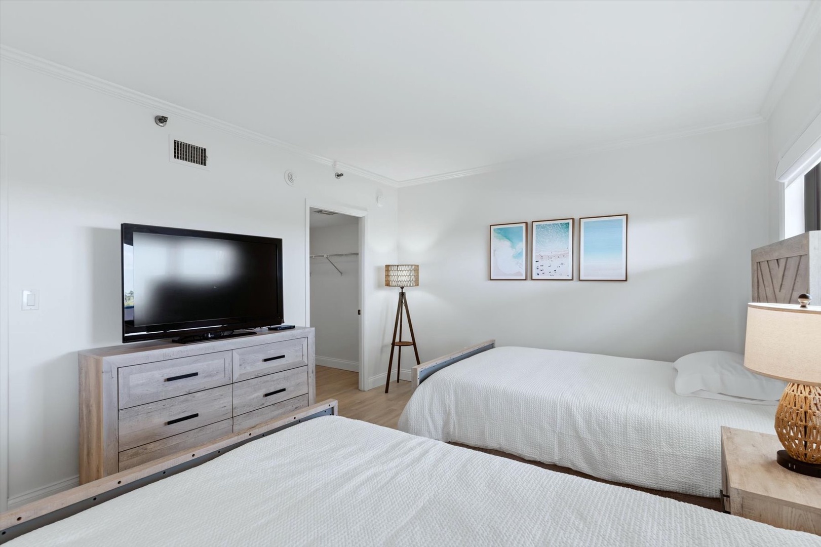 Unwind in your bright, modern bedroom featuring two comfortable beds, a large TV, and soothing coastal artwork that sets the perfect beachy mood.