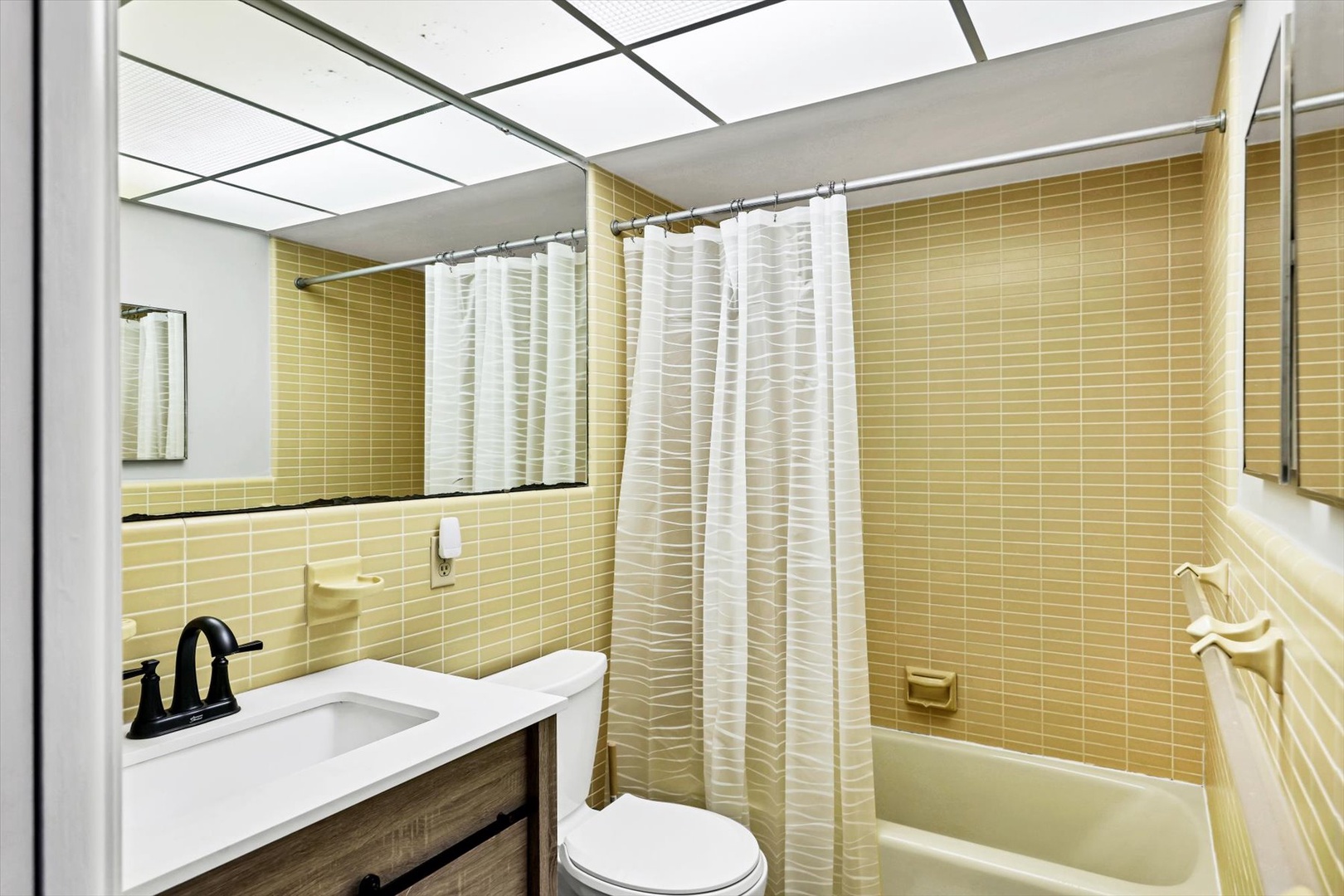 Refresh in your bright bathroom featuring a spacious tub-shower combo with golden tile walls and modern vanity.