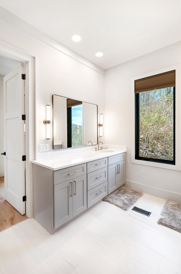 Refresh in your pristine bathroom with sleek vanity, elegant lighting, and peaceful garden views through the window.