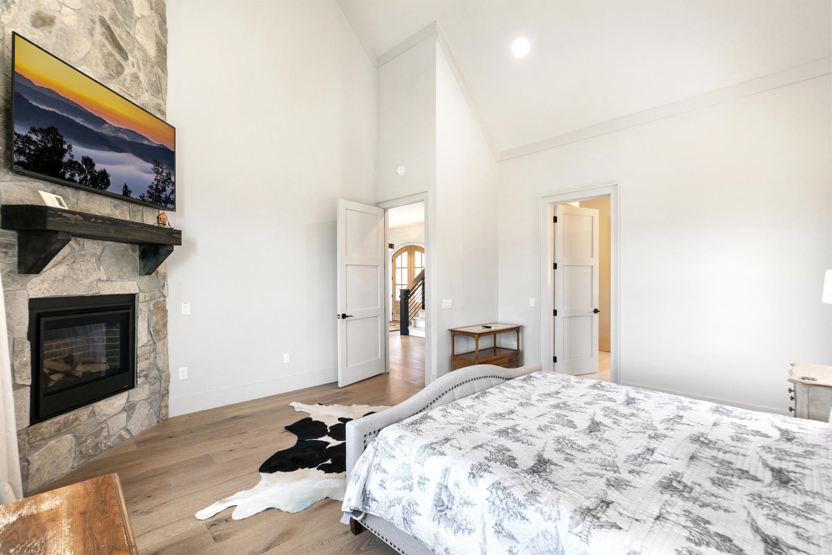 Unwind in your elegant bedroom featuring a cozy stone fireplace, vaulted ceilings, and warm hardwood floors for the perfect retreat.