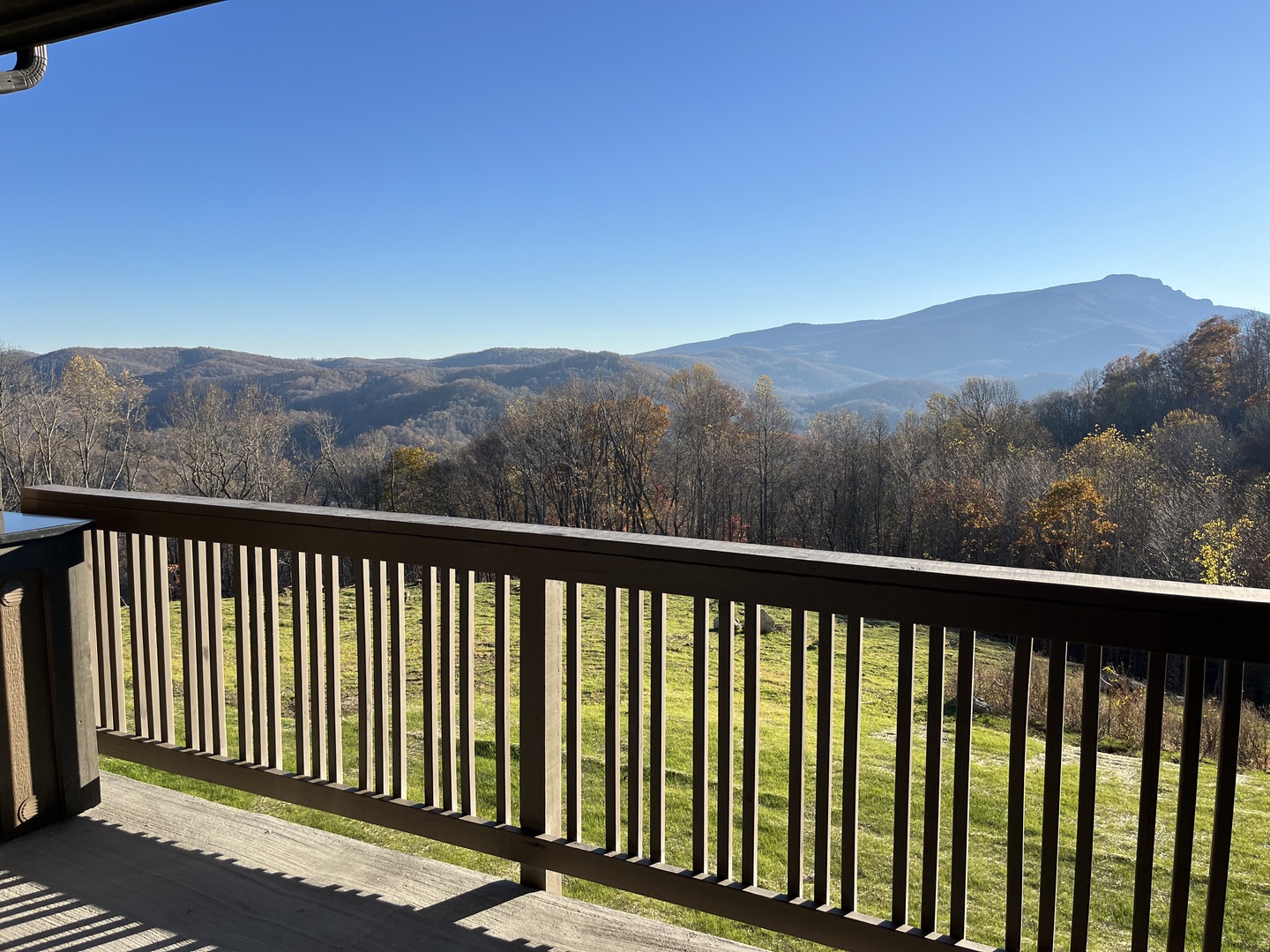 Panoramic mountain views stretch across the horizon from this spacious balcony. Layered peaks and autumn foliage create a peaceful backdrop under a clear blue sky.
