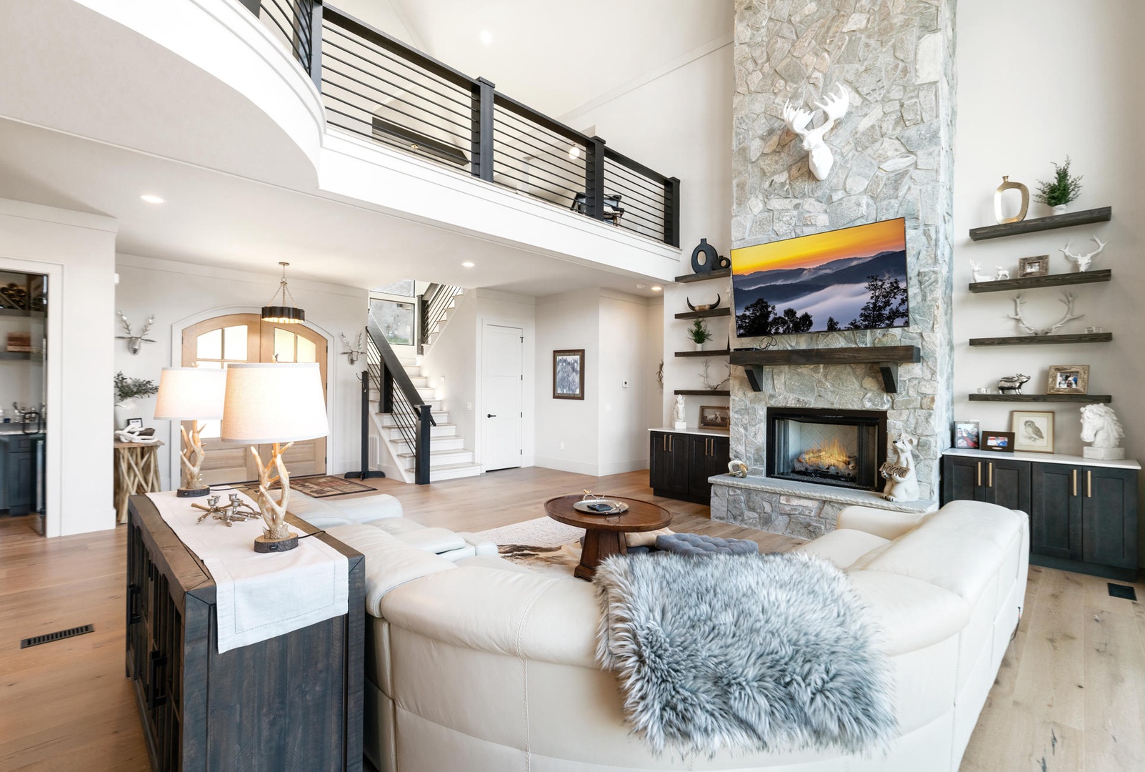 Unwind in your stunning two-story living space featuring soaring ceilings, cozy stone fireplace, and elegant furnishings perfect for relaxation.