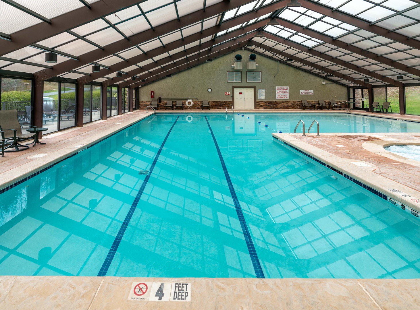 An enclosed swimming pool with clear turquoise water and swim lanes invites you to take a refreshing dip year-round under the bright glass ceiling. Natural light floods the space while windows reveal the surrounding landscape.