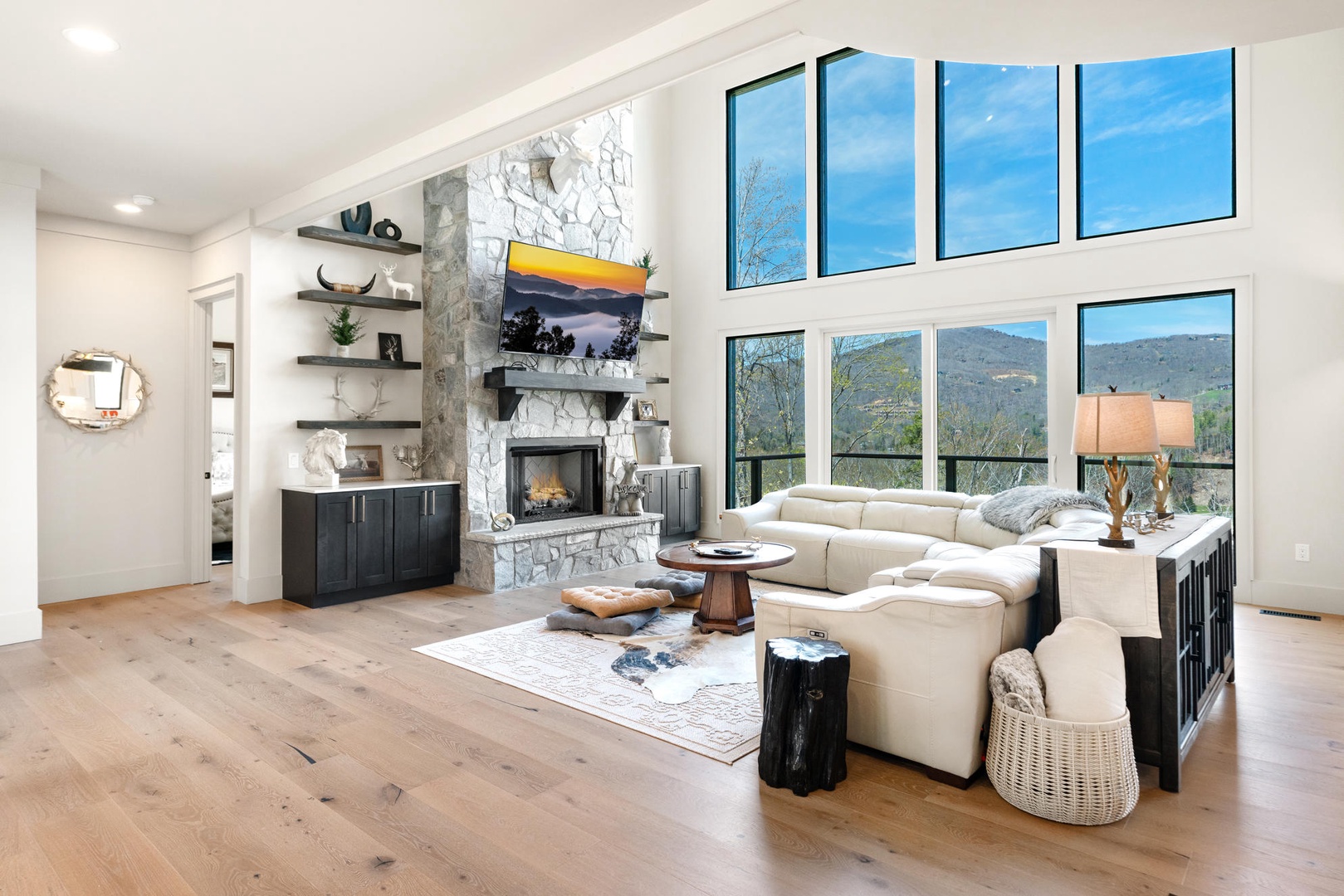Unwind in your spacious living room featuring a cozy stone fireplace and stunning floor-to-ceiling mountain views through panoramic windows.